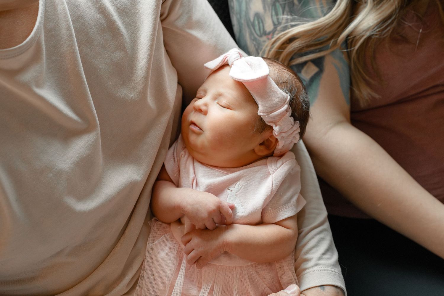 Newborn baby in pink outfit being cradled gently against white bedding.