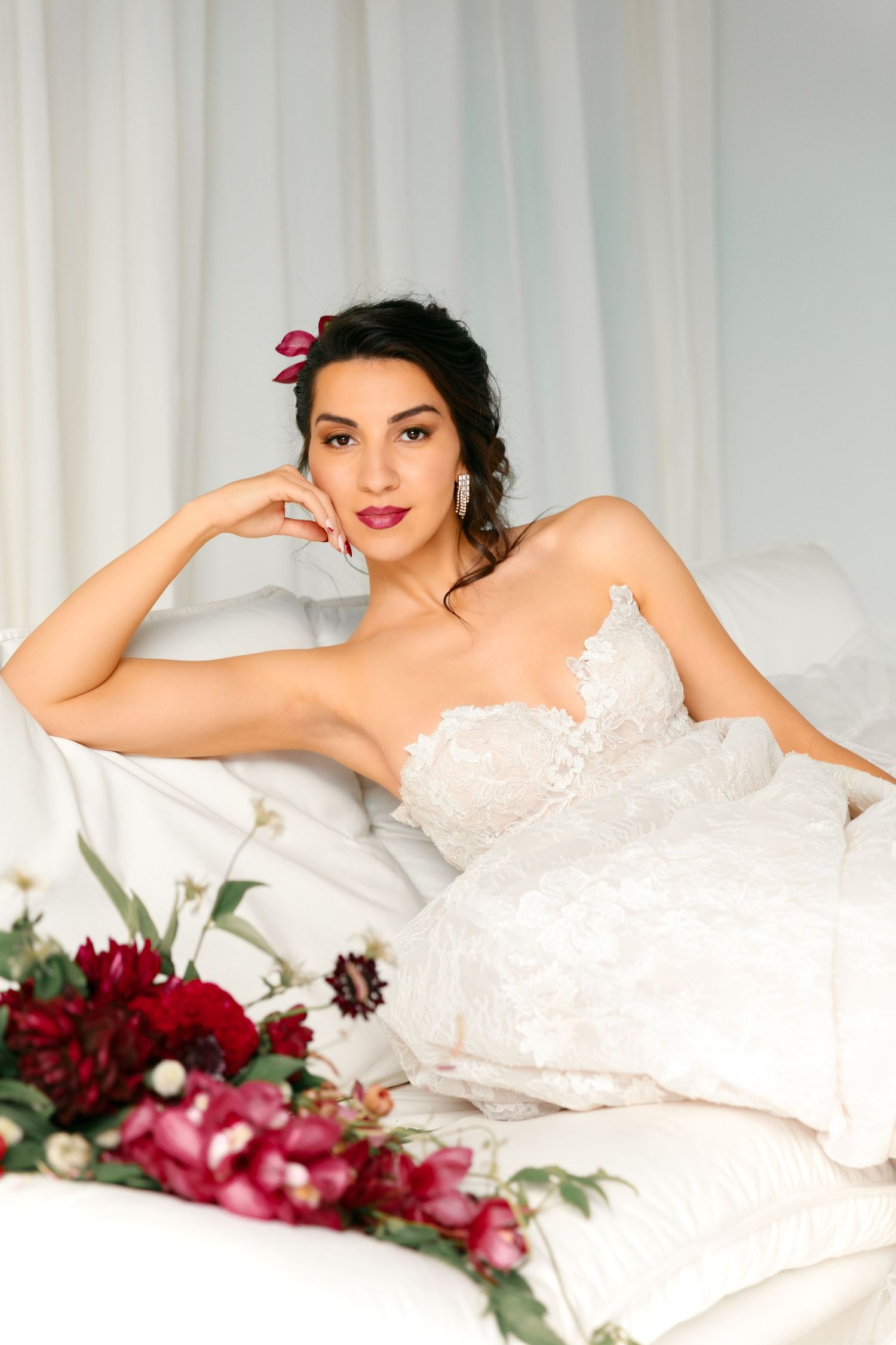 Romantic boudoir session with lace dress, red flowers and soft white bedding.