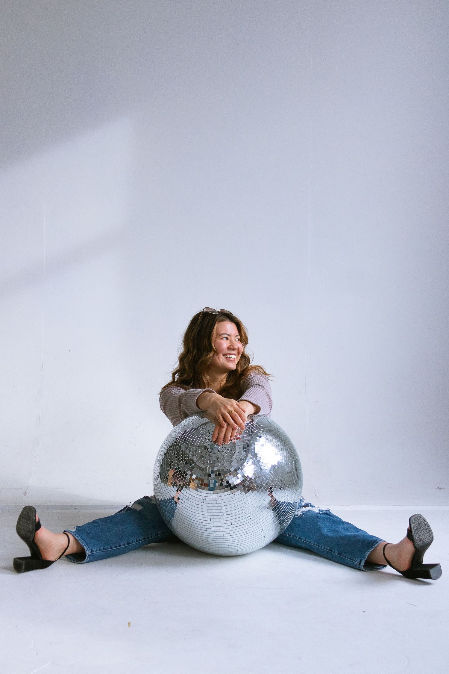 Casual portrait with model sitting on floor embracing large silver disco ball.