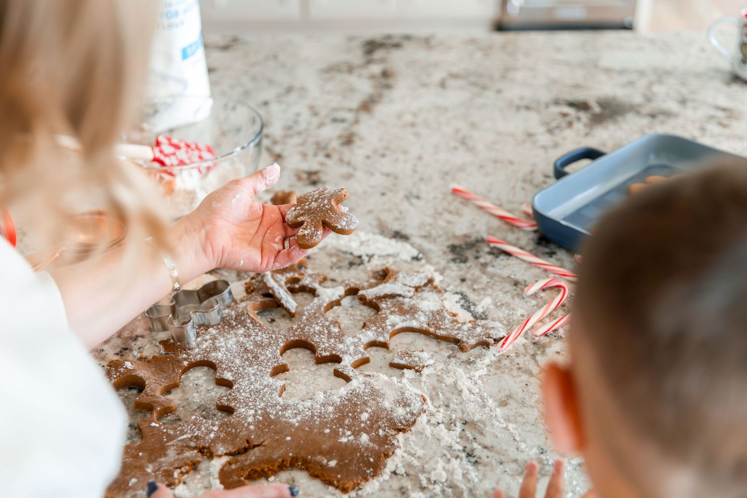 Children cutting gingerbread cookie shapes from dough on a flour-dusted counter during holiday baking.