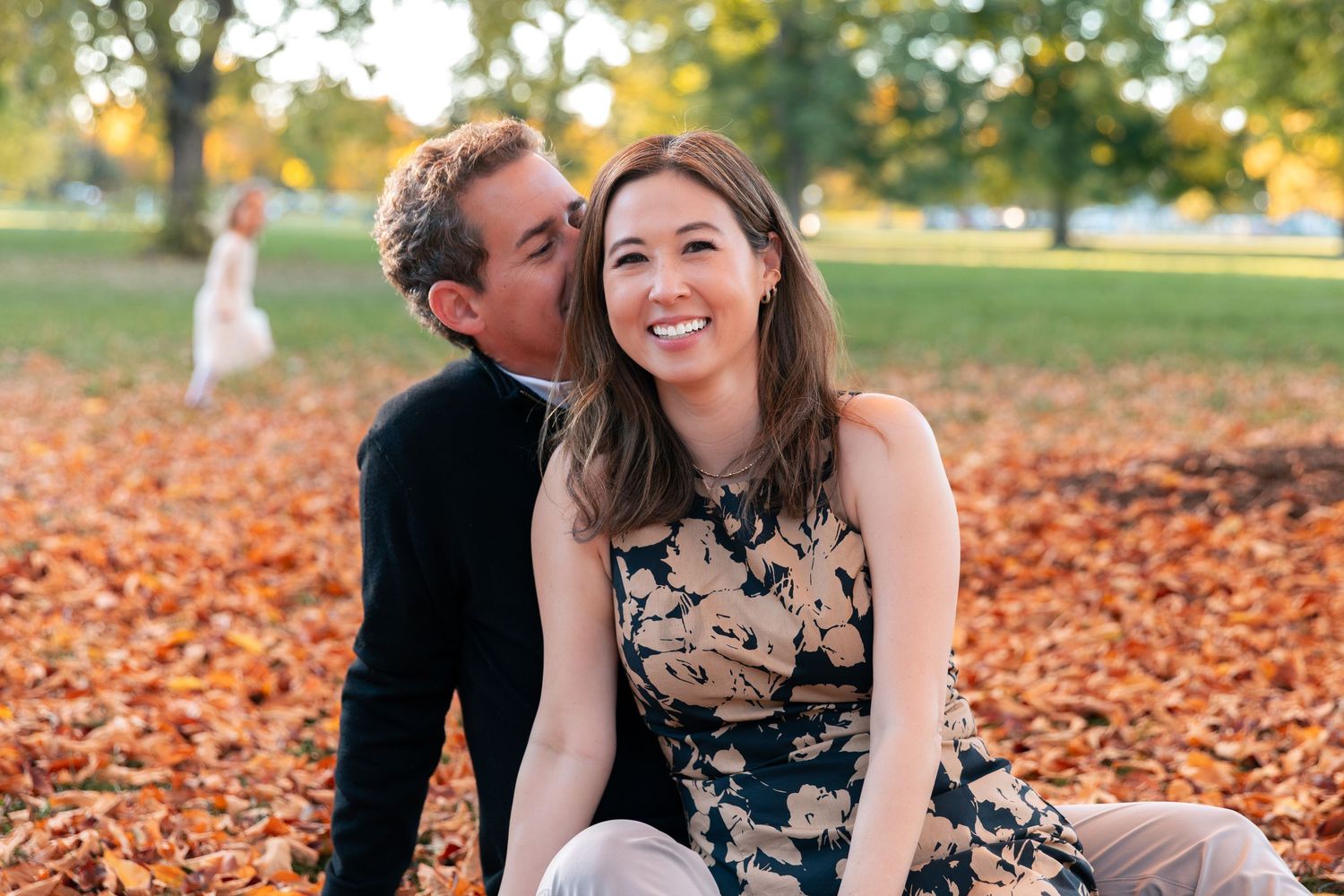 Couple laughing together while lying in autumn leaves during outdoor photo session.