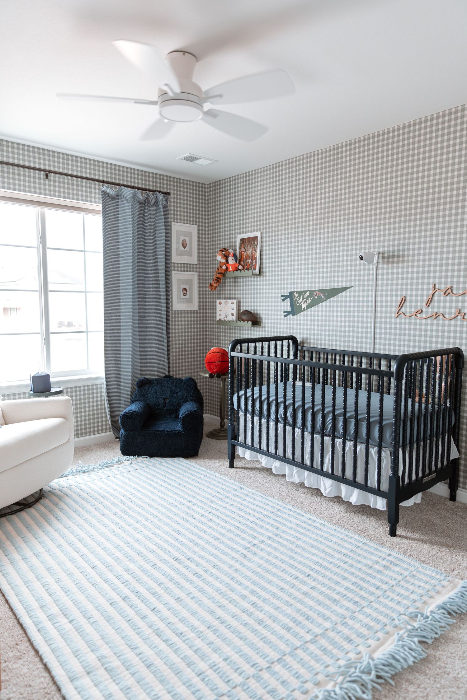 Modern nursery with black crib, gingham wallpaper, and navy accent chair.