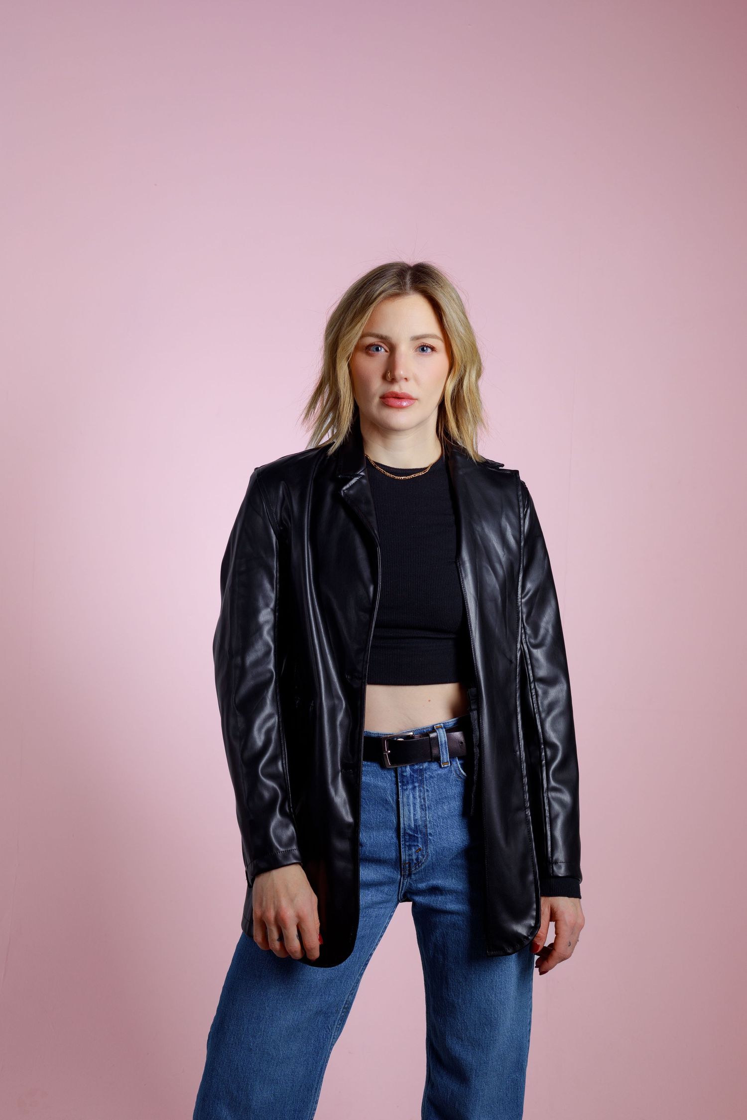 Person modeling black leather jacket and jeans against pink studio background.