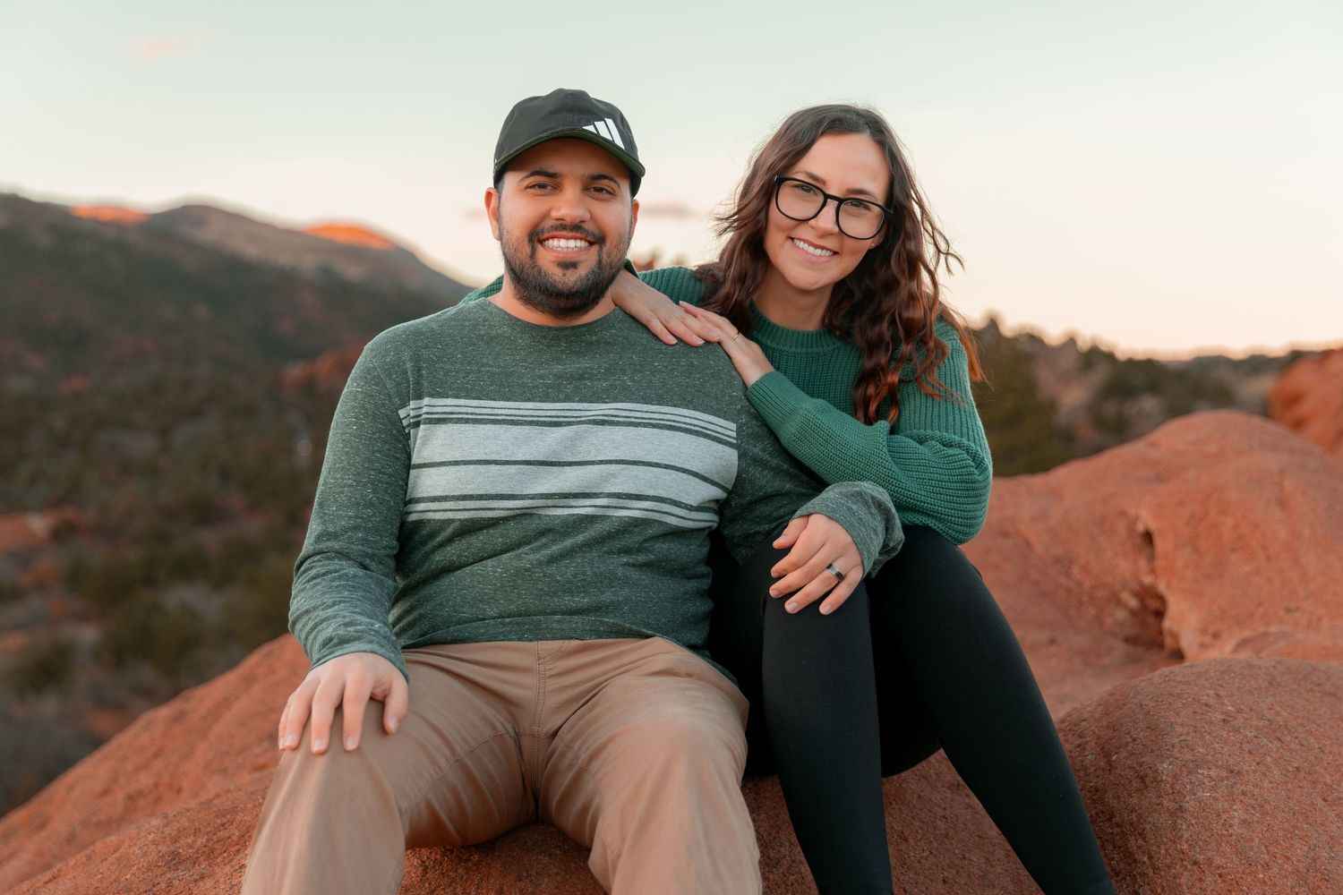 A couple poses together at sunset on red rock formations in a desert landscape.