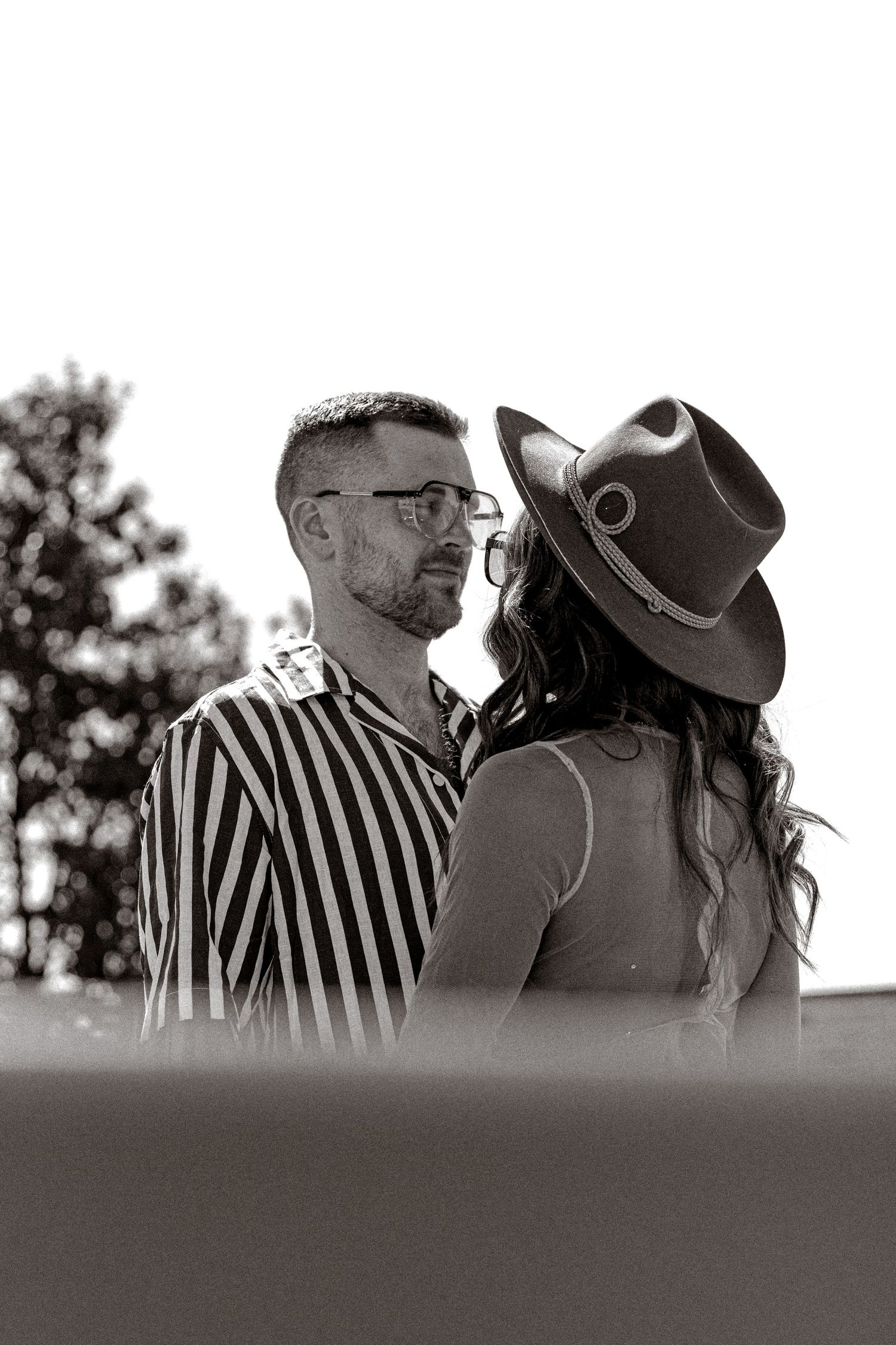 Romantic black and white photo of couple in striped shirt and hat embracing outdoors.