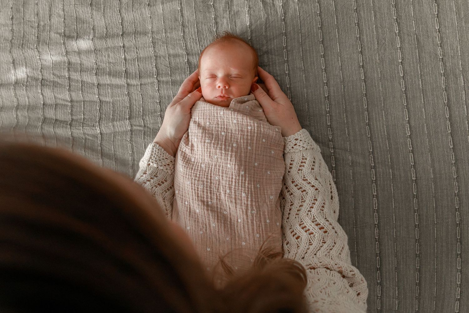 Baby wrapped in white textured blanket on grey bedding.