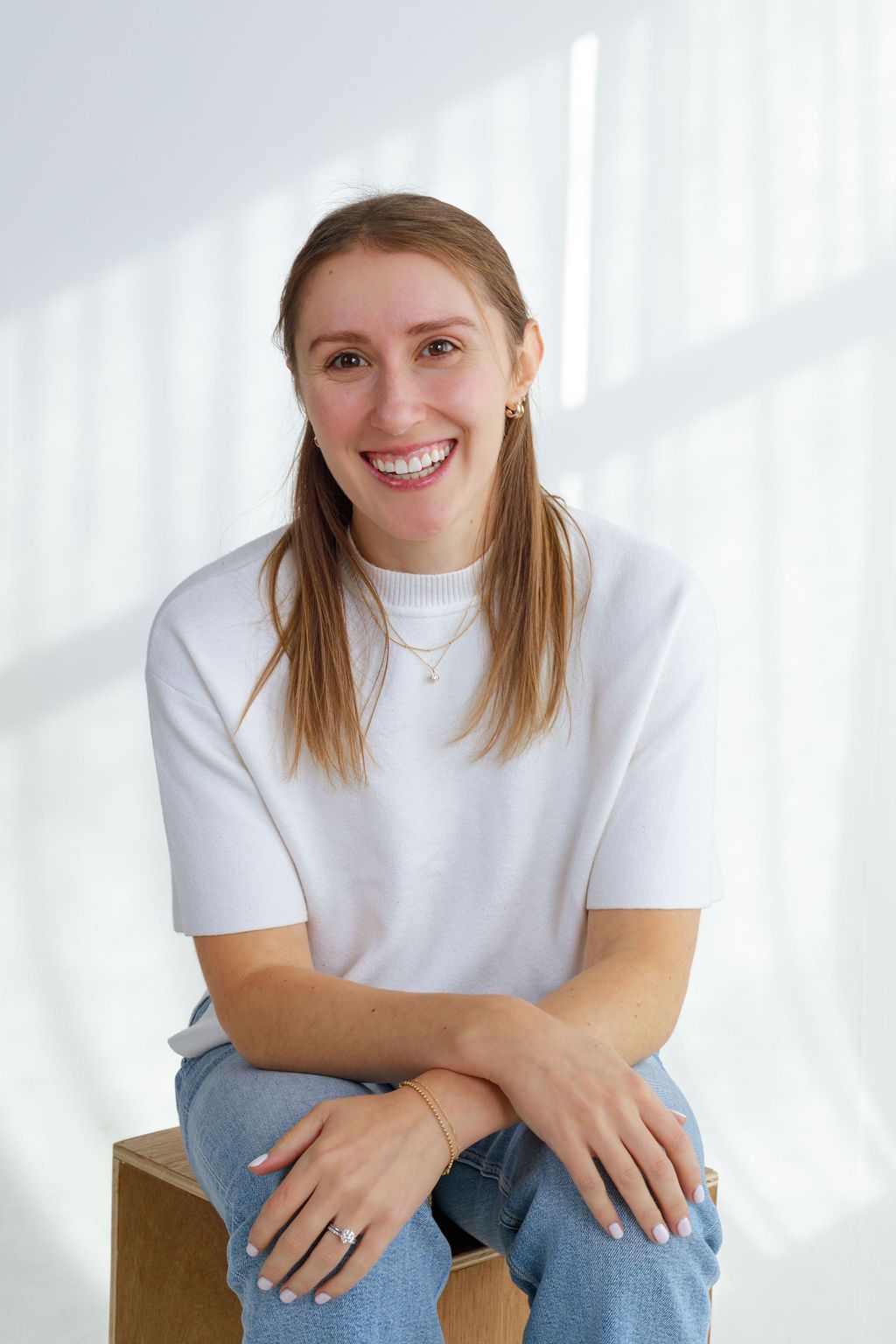 Portrait of someone in a white t-shirt and jeans sitting on a wooden box against a white background.
