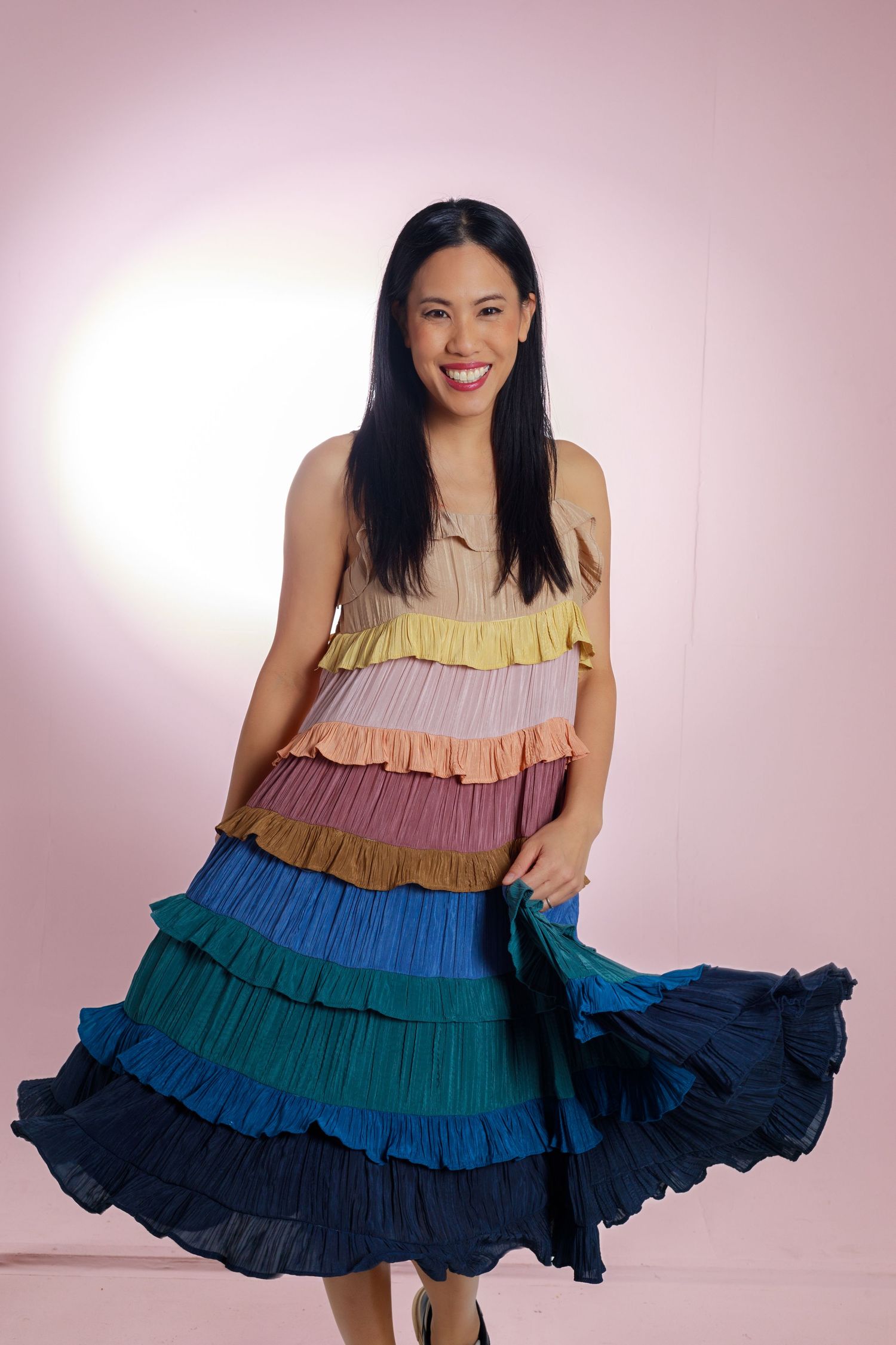 Person wearing colorful tiered ruffle dress twirls against pink backdrop.