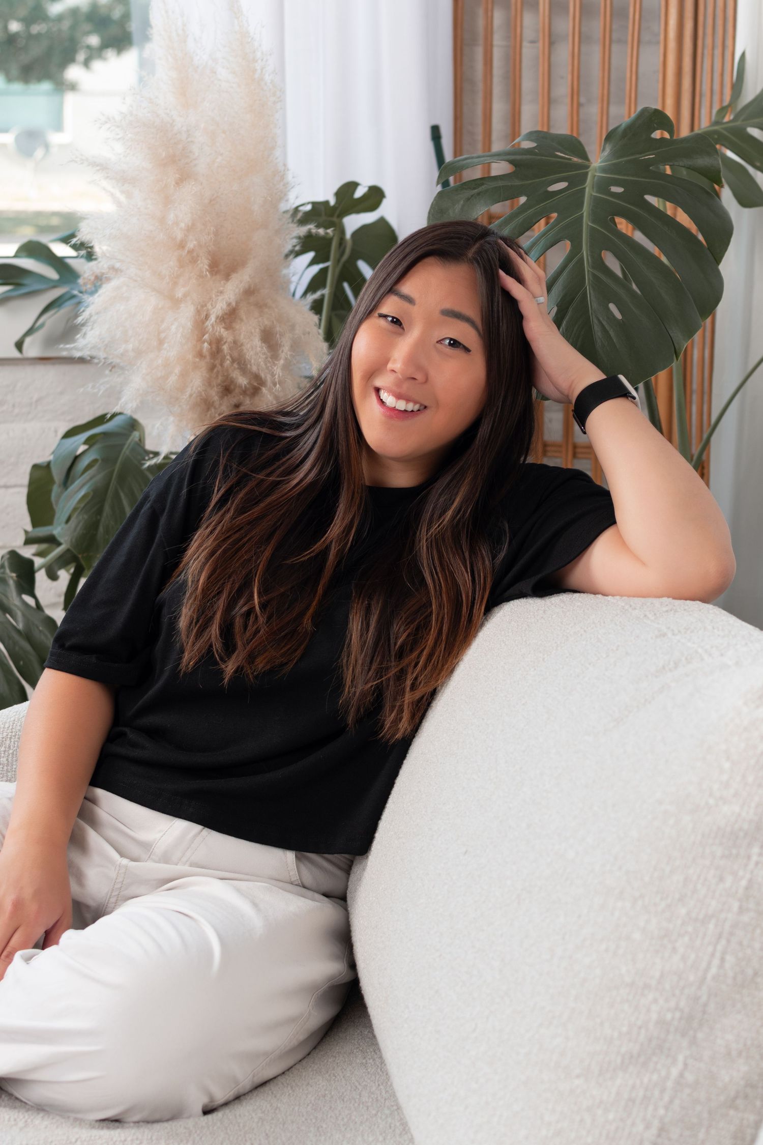 Person relaxing on white couch with monstera leaves and pampas grass decor.