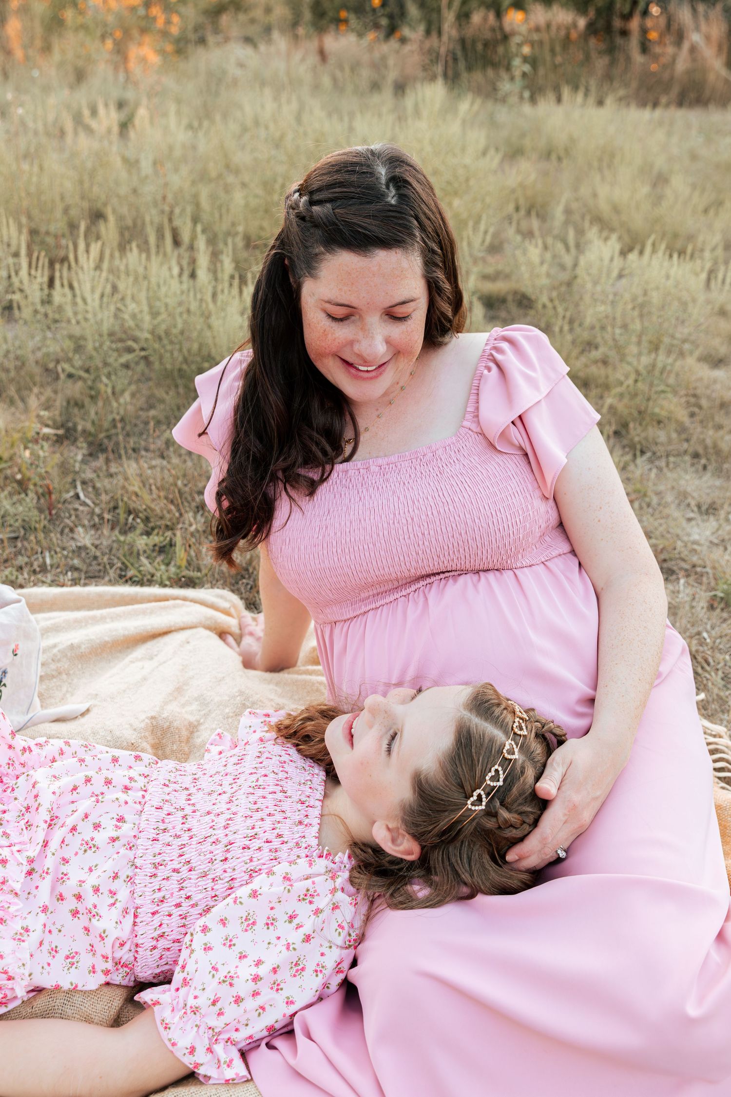 A tender mother-daughter moment captured during a pink-themed outdoor photoshoot in a field.