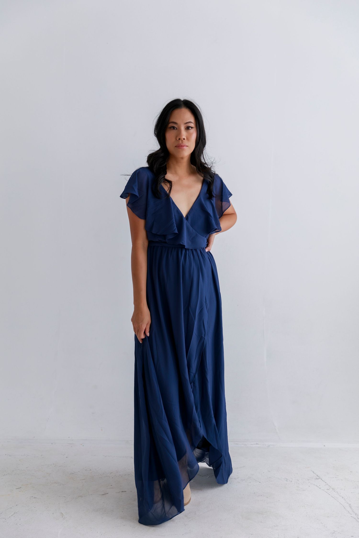 Navy blue flutter sleeve wrap dress with v-neckline and flowing maxi length skirt.
