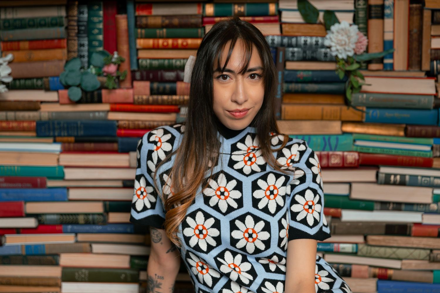 Woman in floral dress poses against colorful bookshelf backdrop in library setting.