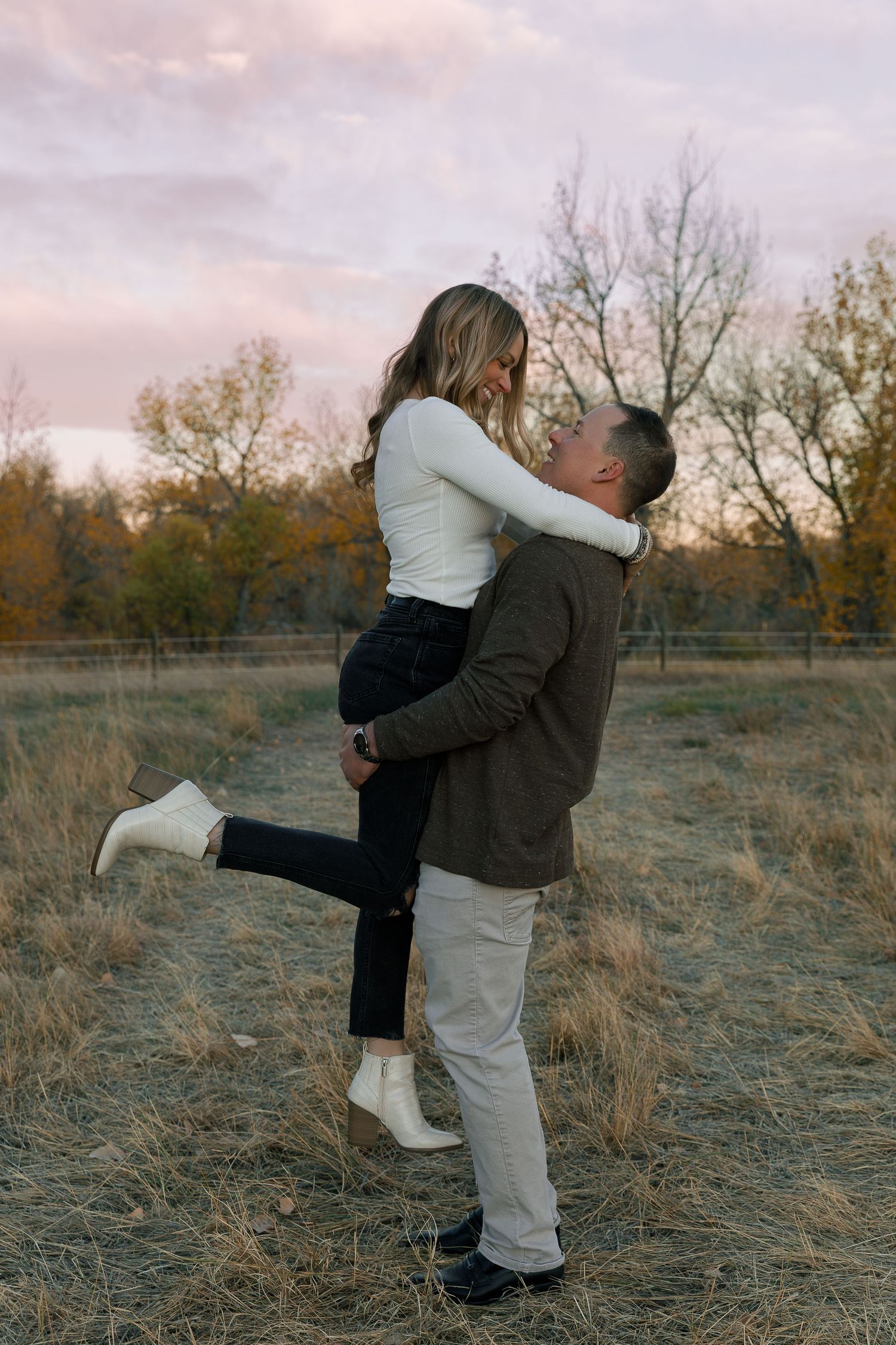 A couple embraces and spins playfully in a field during sunset.