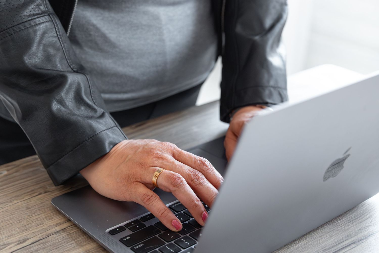 Close-up of hands typing on a MacBook keyboard on a wooden desk.