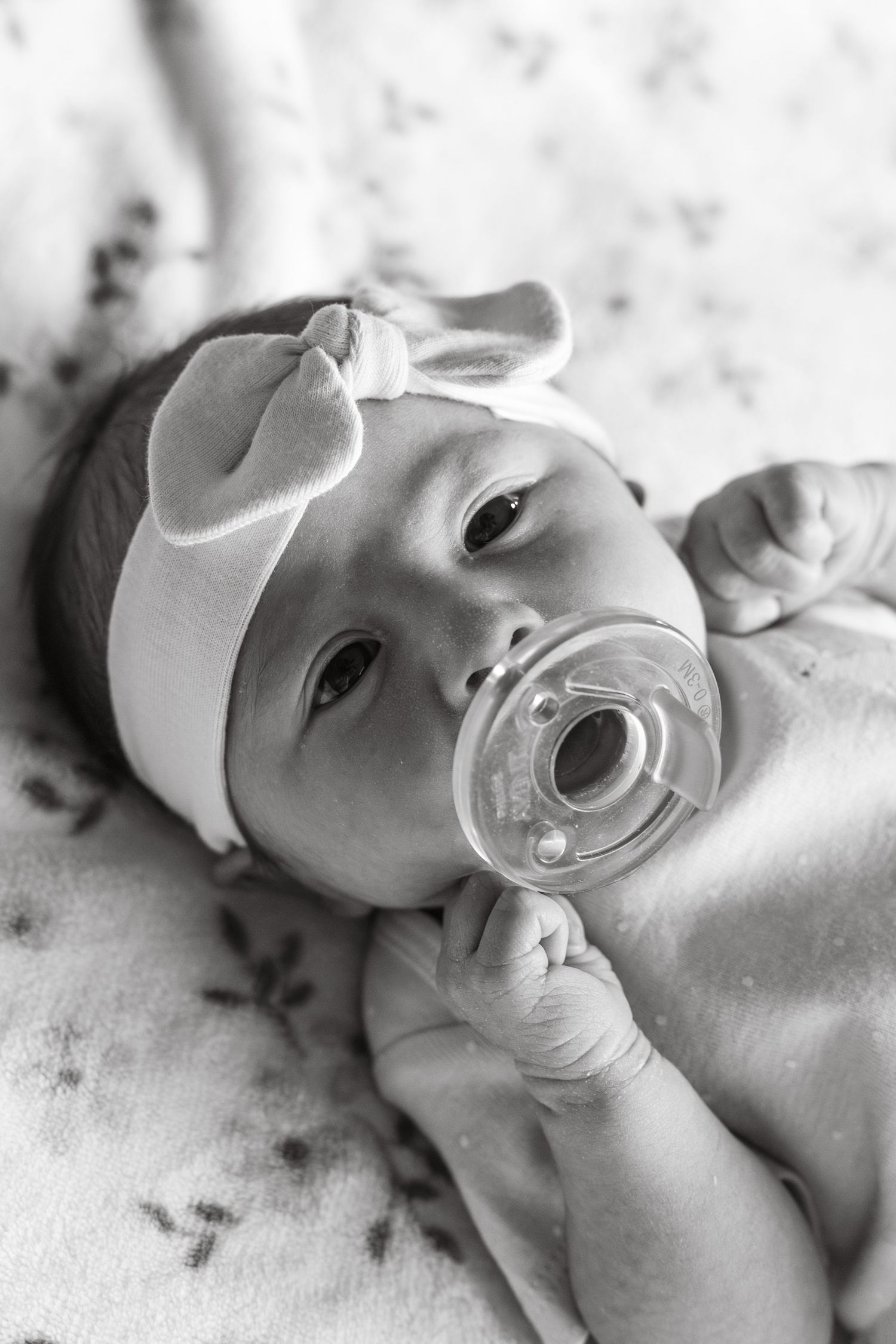 Black and white portrait of a newborn baby with pacifier wearing a light colored cap.
