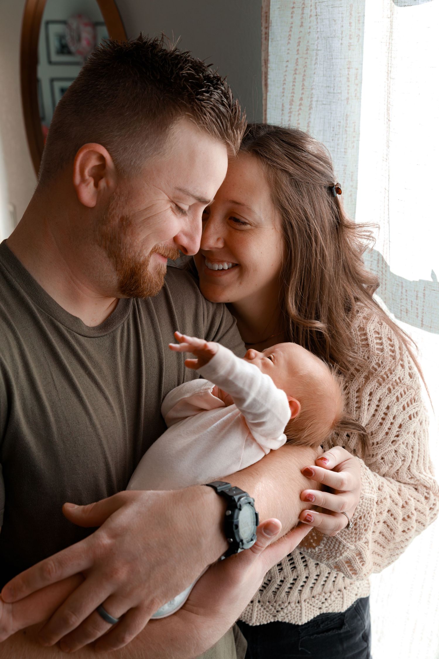 Intimate family moment with newborn baby by window light.