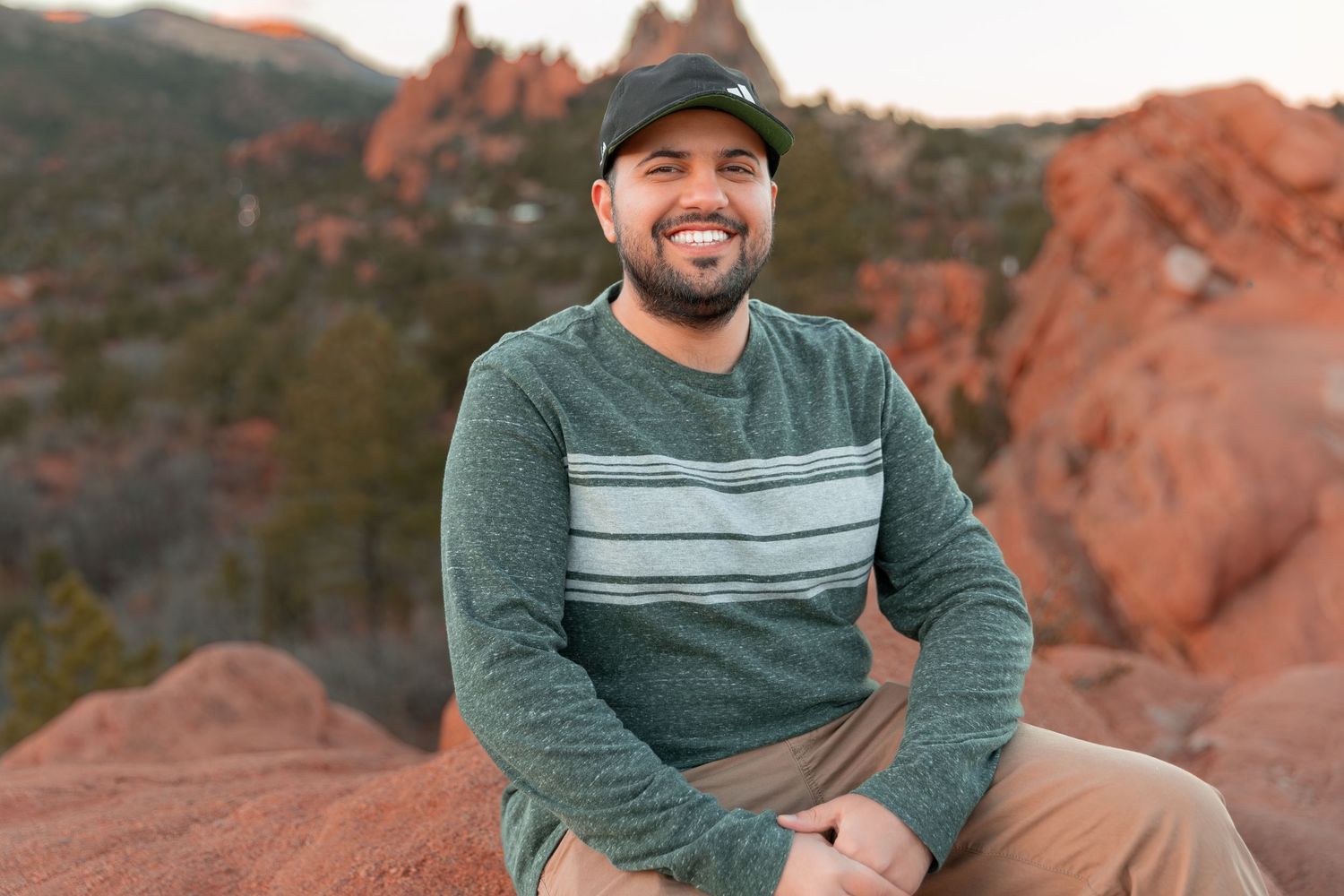 Person in casual attire sitting on red rock formations during sunset.
