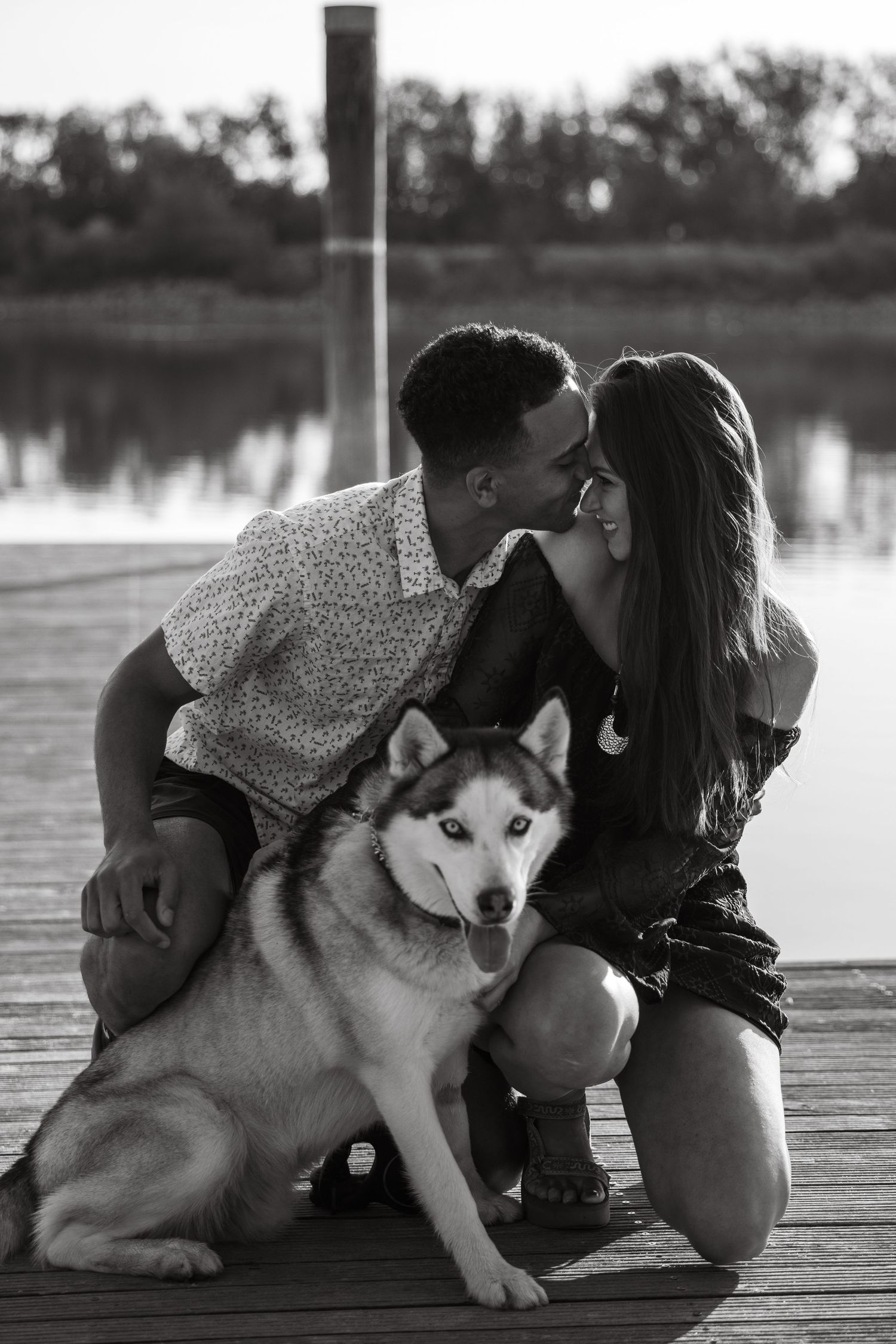 A husky dog and person share a quiet moment together on a wooden dock by the water.