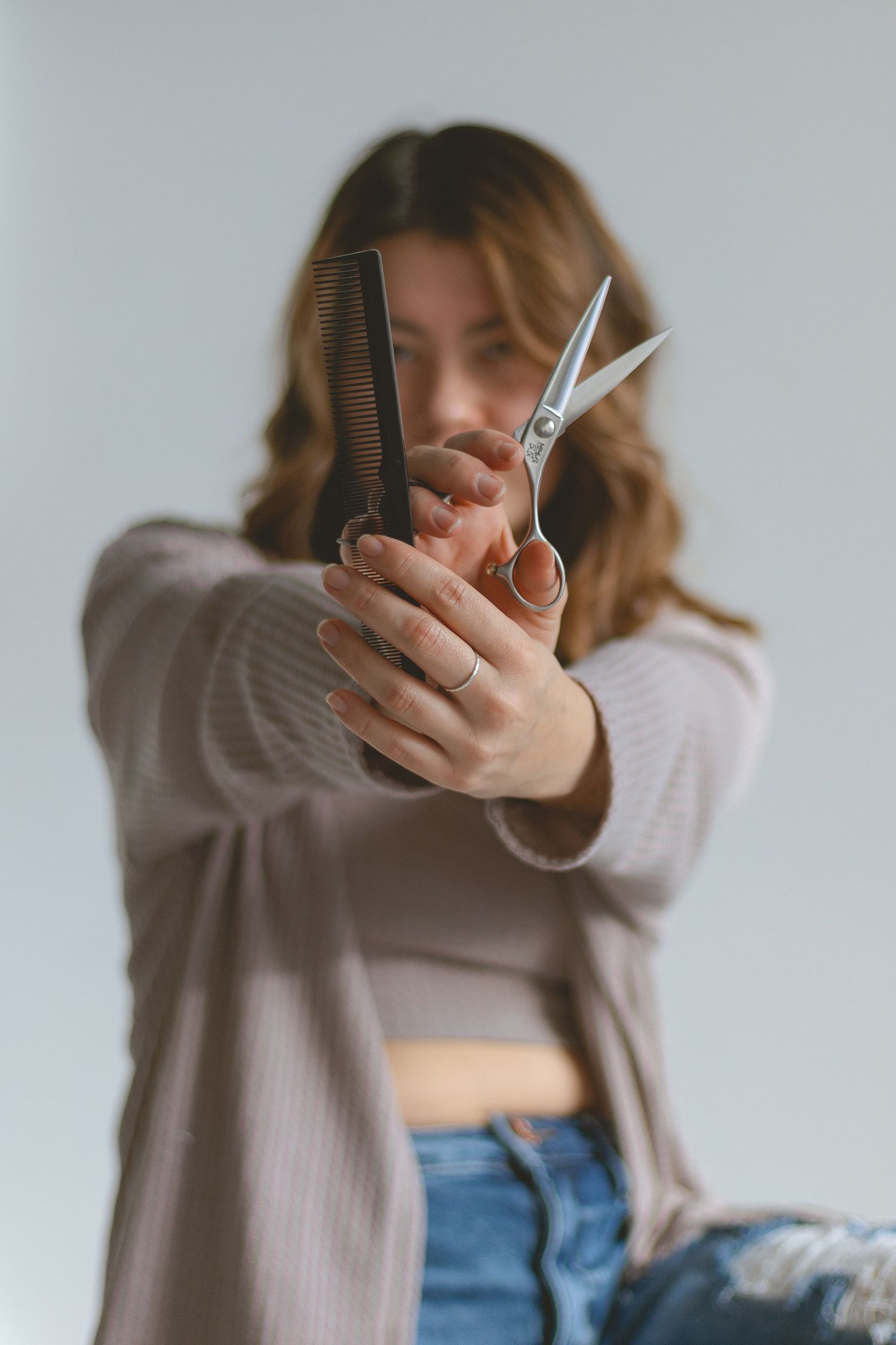 Close-up shot of hands holding hairdressing scissors and comb against light background.