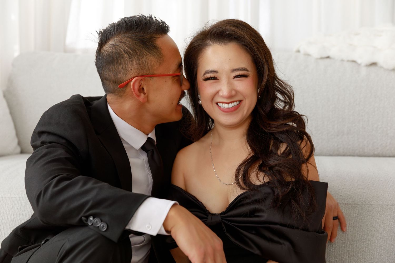 Intimate holiday portrait session with couple embracing on white couch near Christmas decorations.