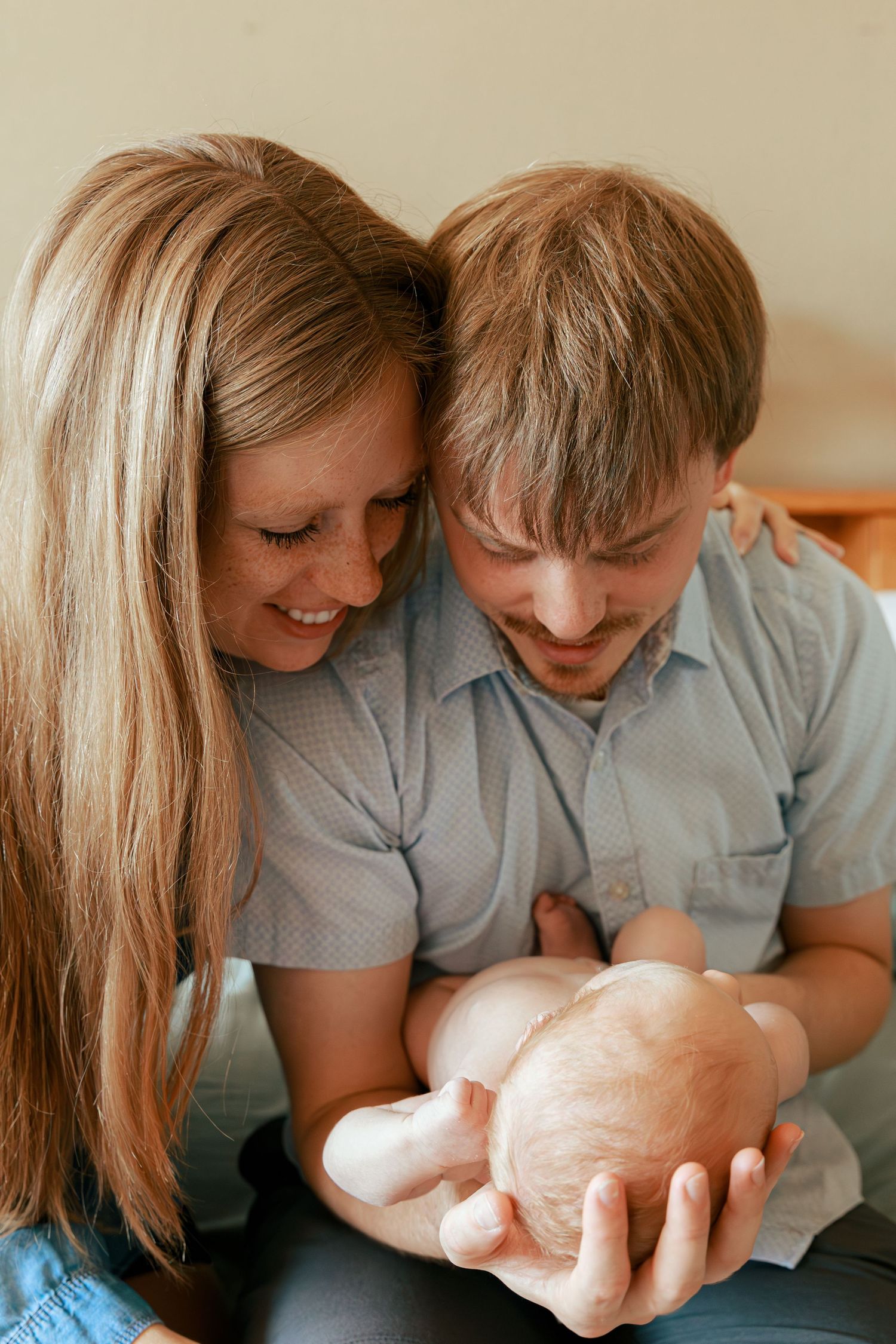 Parents in matching gray shirts lovingly gaze at their newborn baby.