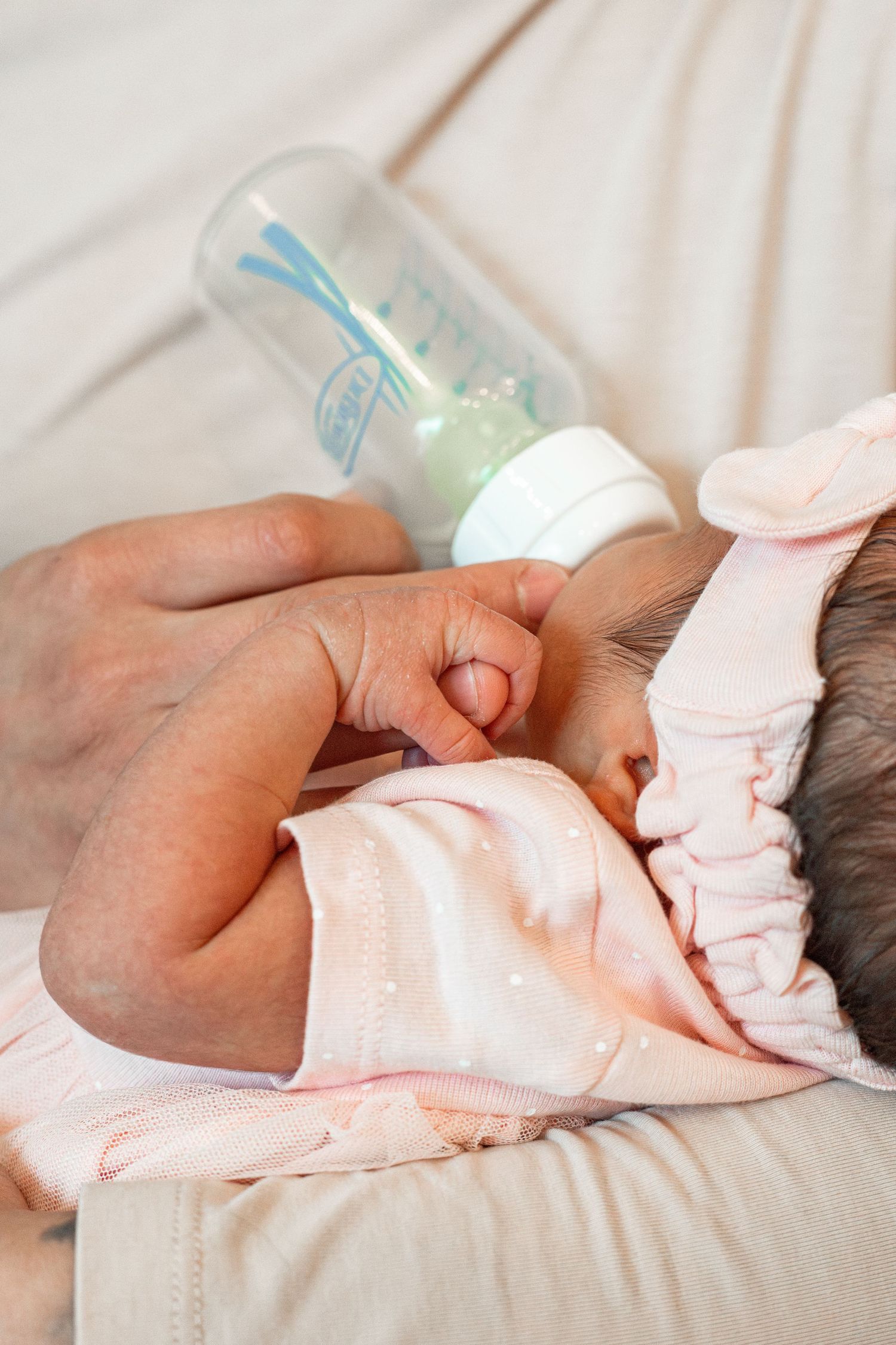 Newborn baby sleeping peacefully in pink outfit while being held by caring hands.