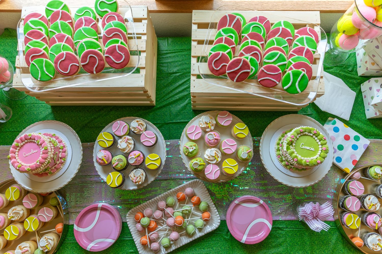 Colorful tennis-themed party dessert table with decorated cookies, cupcakes, and cakes in pink and green.