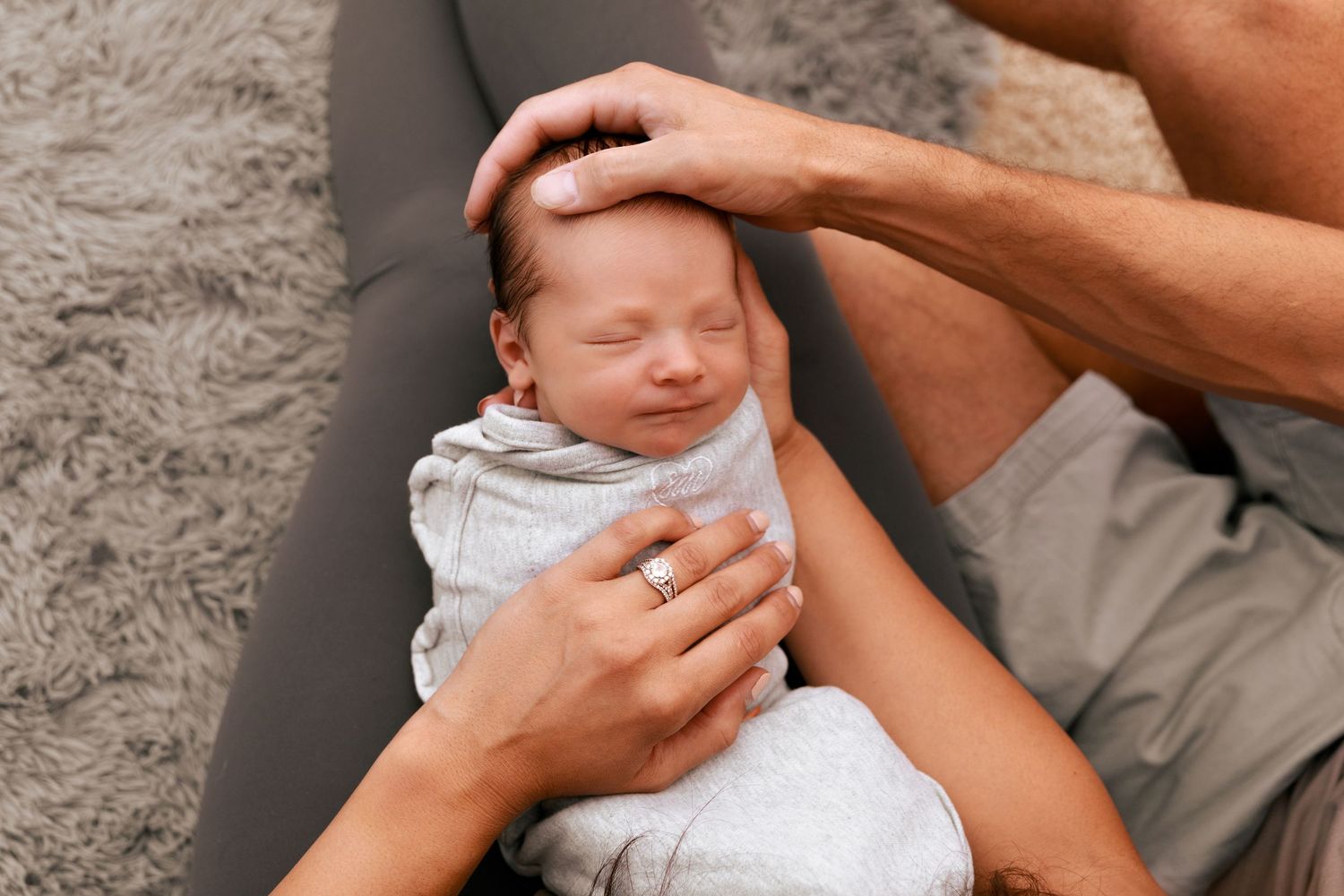 Tender moments captured of hands cradling newborn baby against gray backdrop.