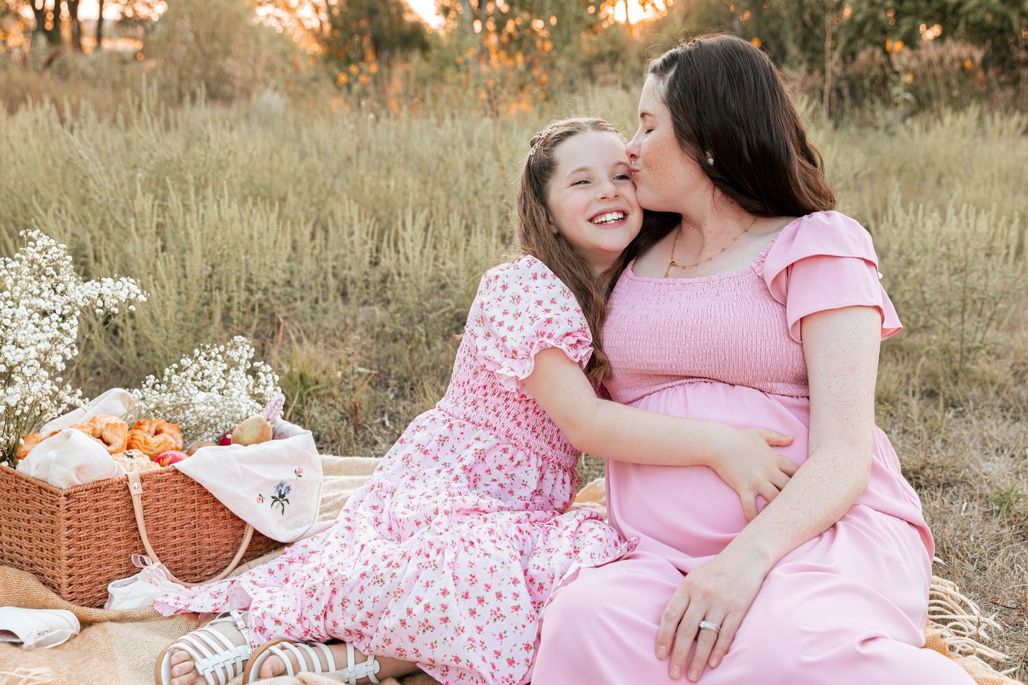 A joyful picnic scene with pink dresses and a wicker basket in a golden field at sunset.