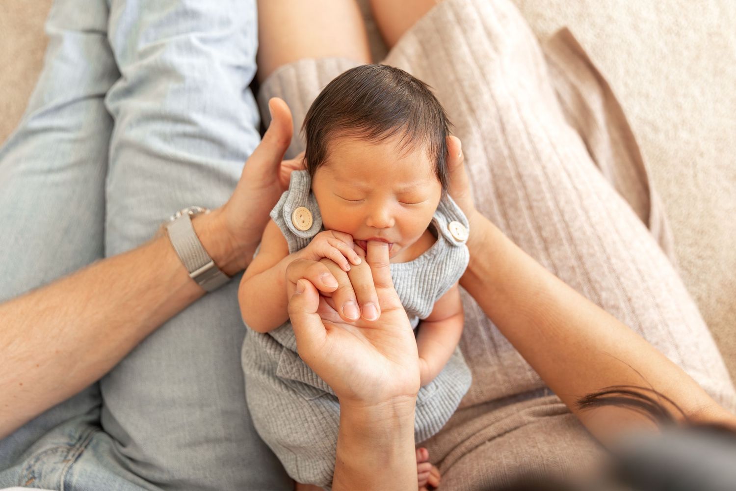 Newborn baby sleeping peacefully in parents' arms, cradled gently between mother and father.