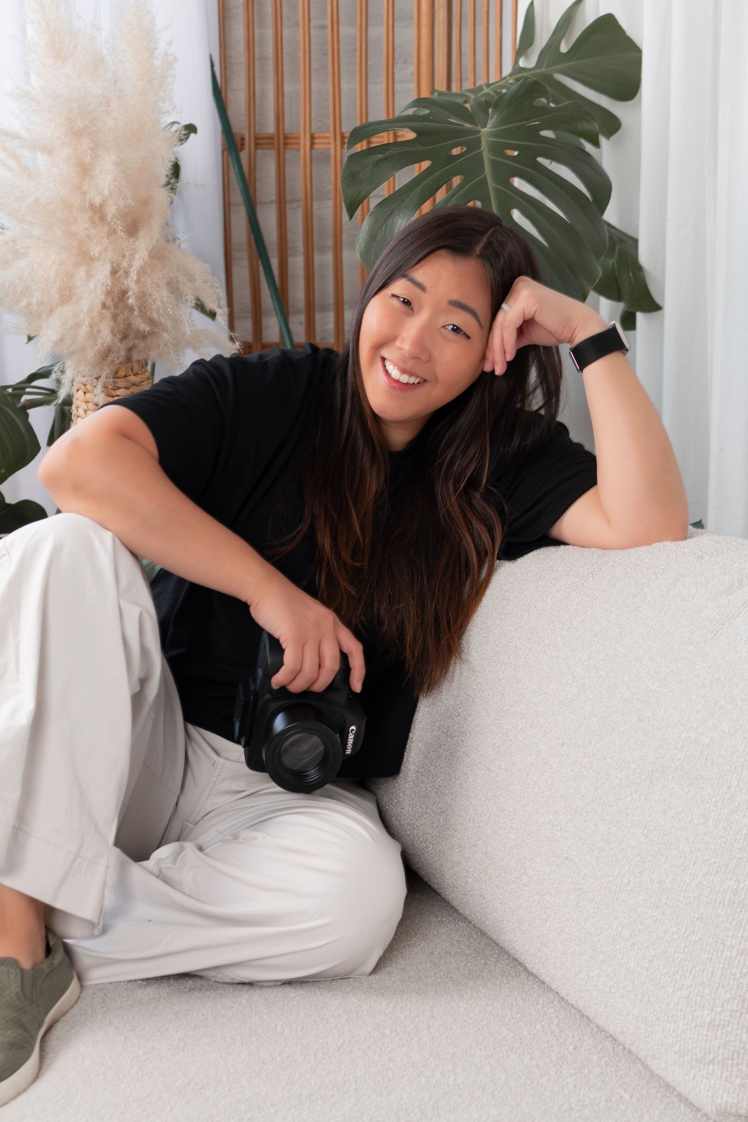 Woman relaxing on white couch with tropical plants and pampas grass decor.