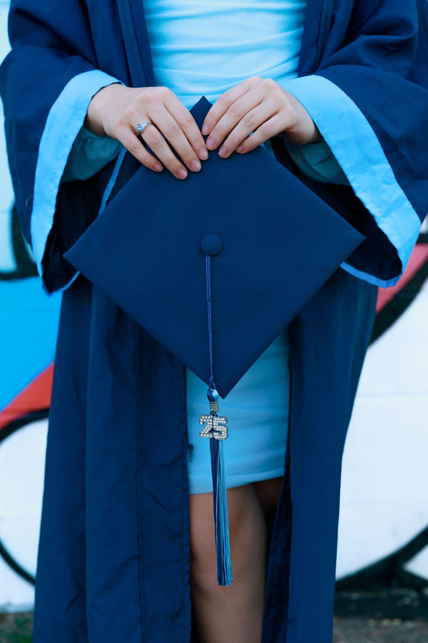 Close-up of graduation cap and tassel against blue graduation gown and vibrant background.