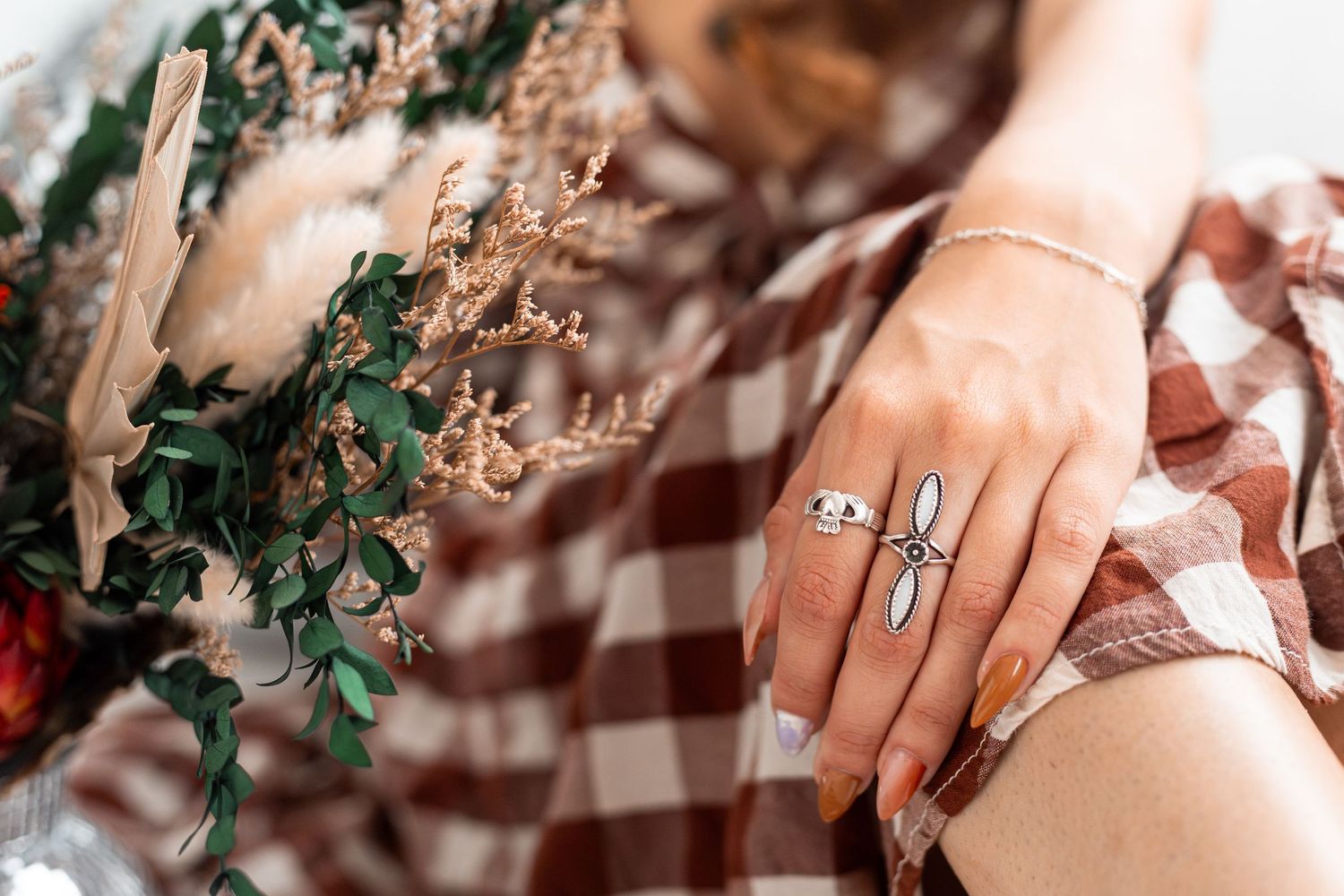 Close-up of hands with rings against brown gingham fabric and greenery.