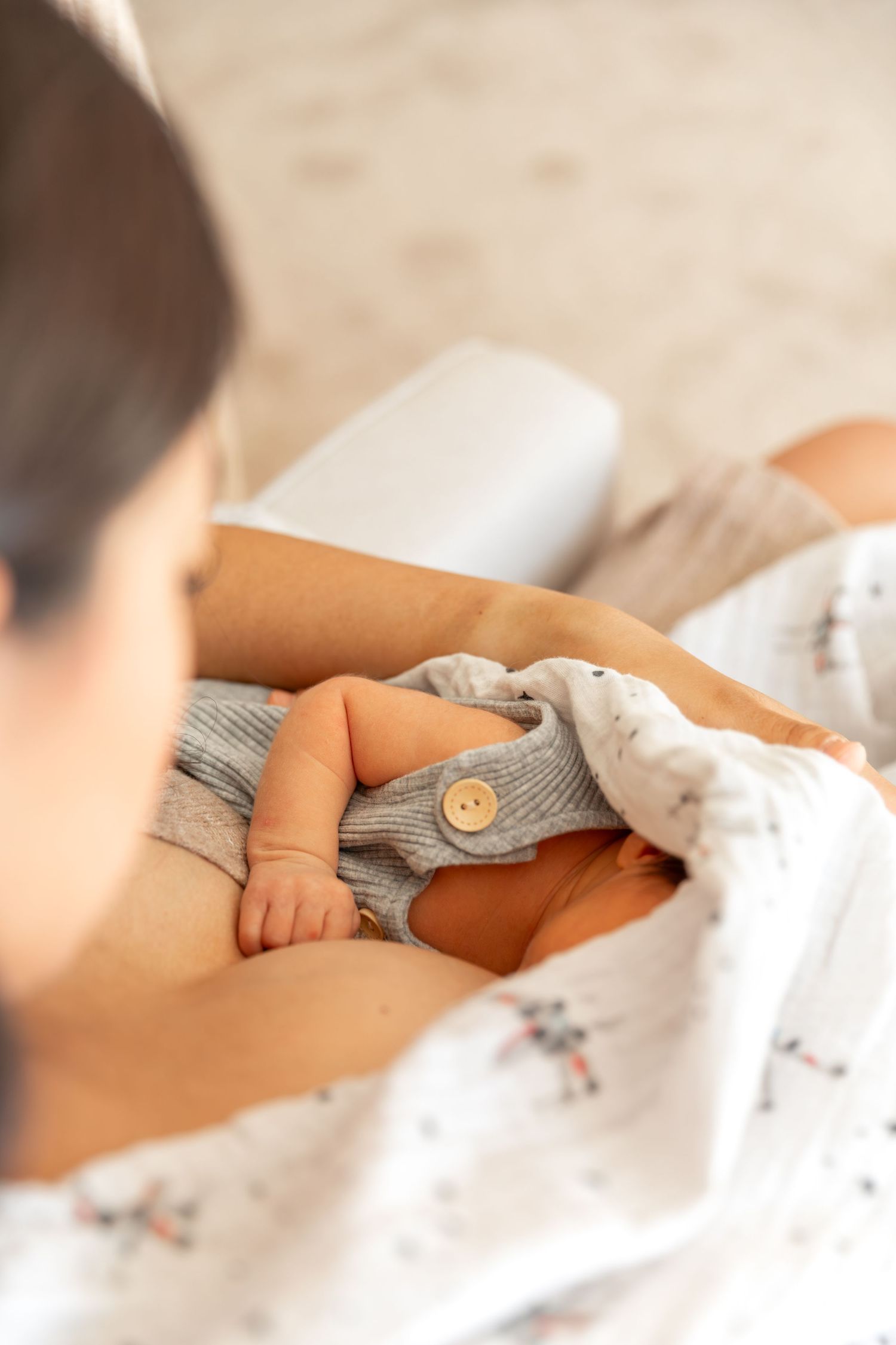 Mother cradling newborn baby dressed in gray ribbed romper with wooden button detail.