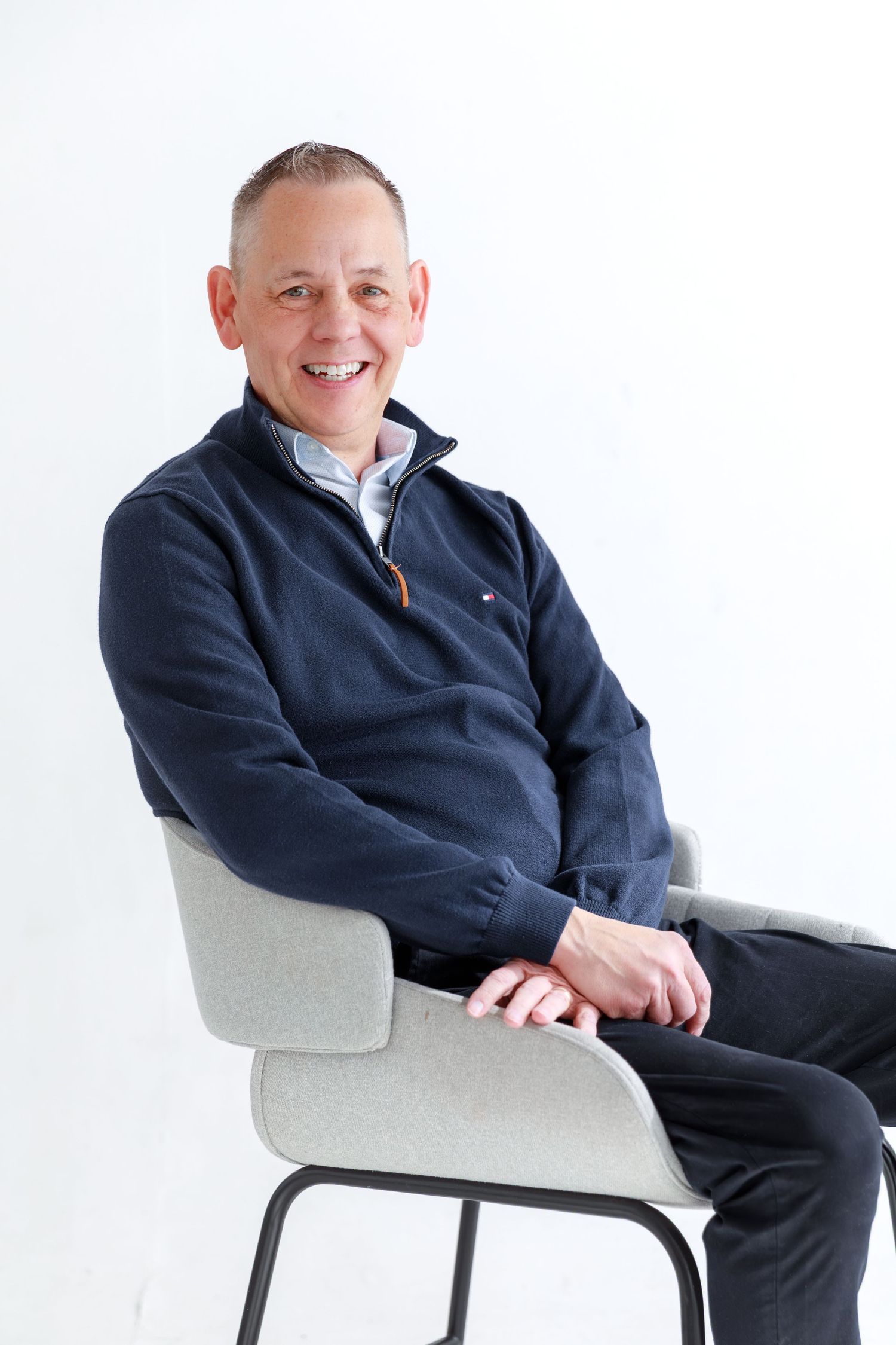 Three identical photos of a person in a navy suit sitting in a modern white chair against a white background.