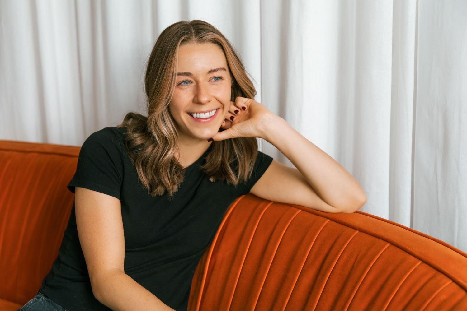 Lifestyle portrait session on orange couch with natural window lighting.