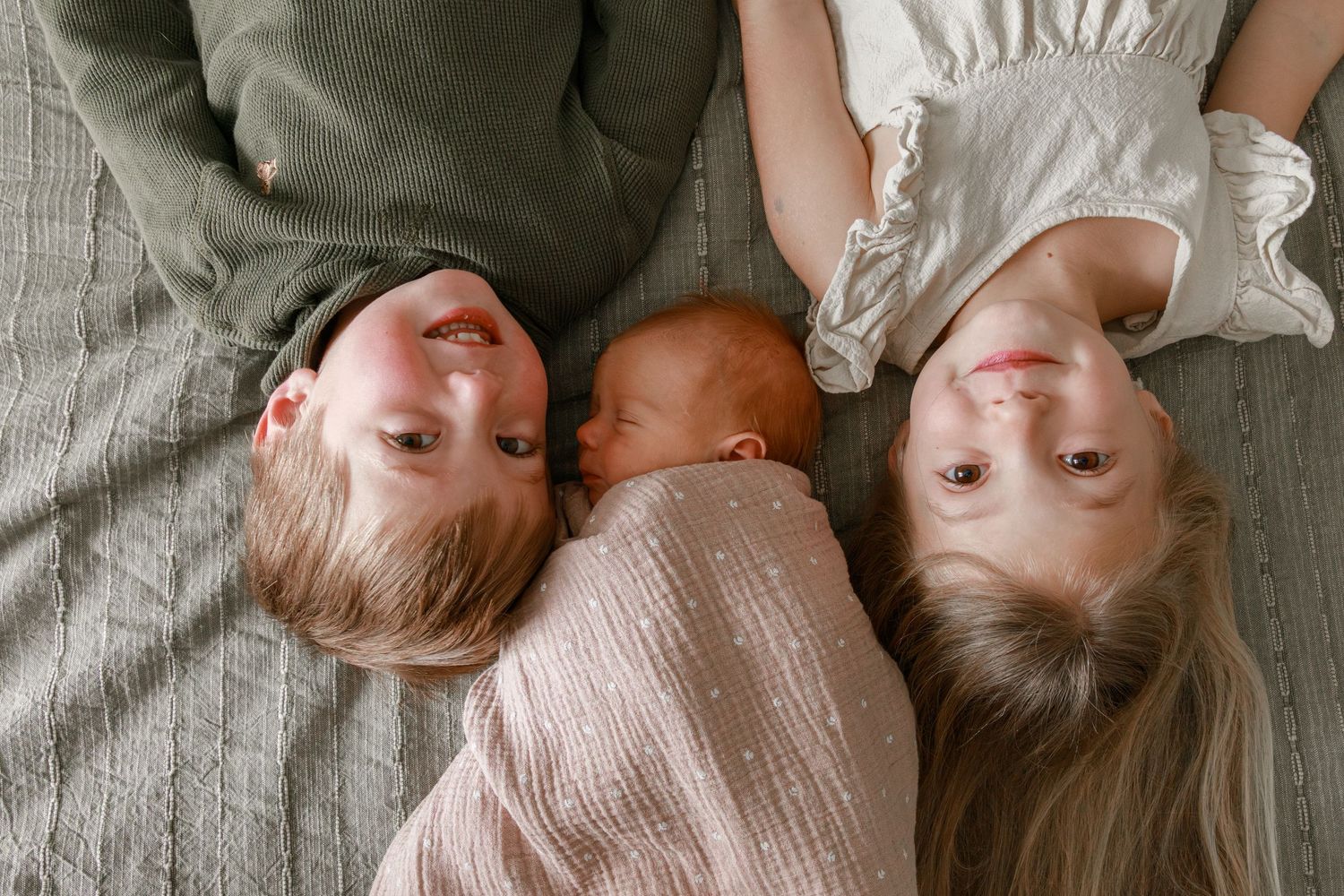 Siblings lying together on gray bedding captured from above.