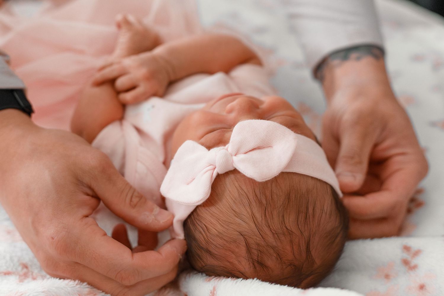 Gentle hands cradling a sleeping newborn baby on soft bedding.