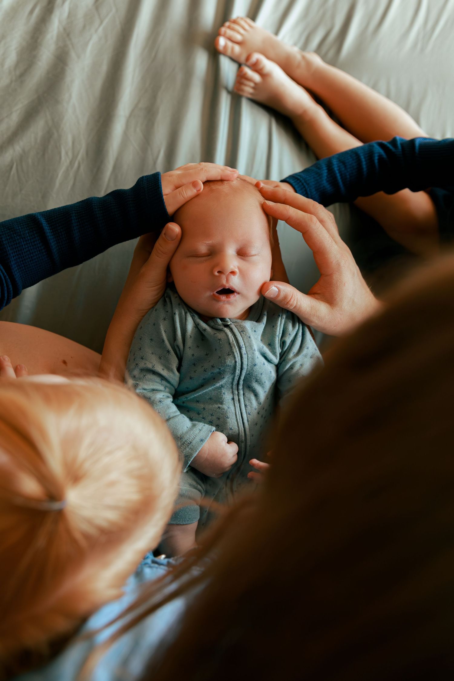 Baby lying on white bedding reaches up playfully during intimate moment.