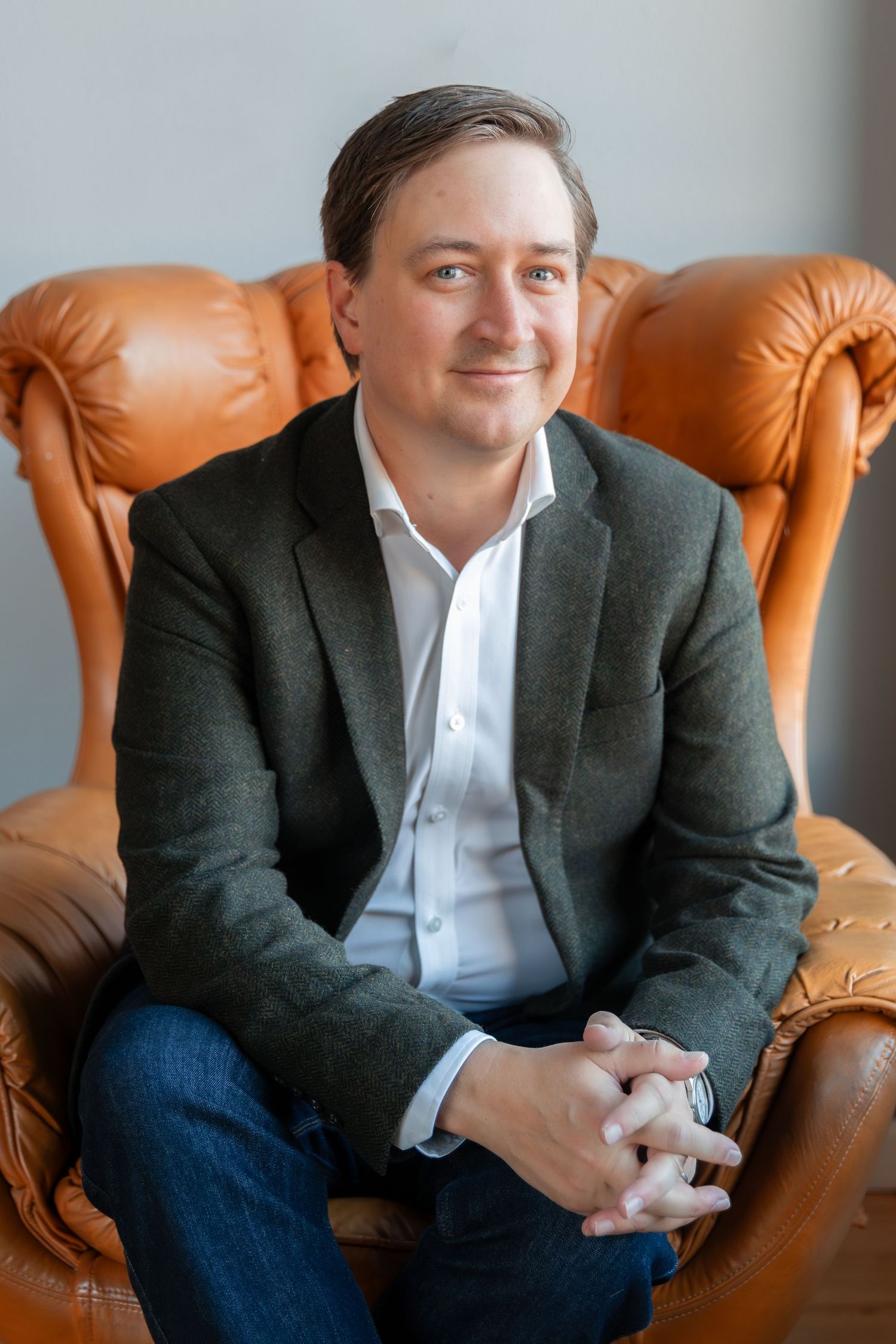 Business professional seated on leather chair in gray blazer and jeans.