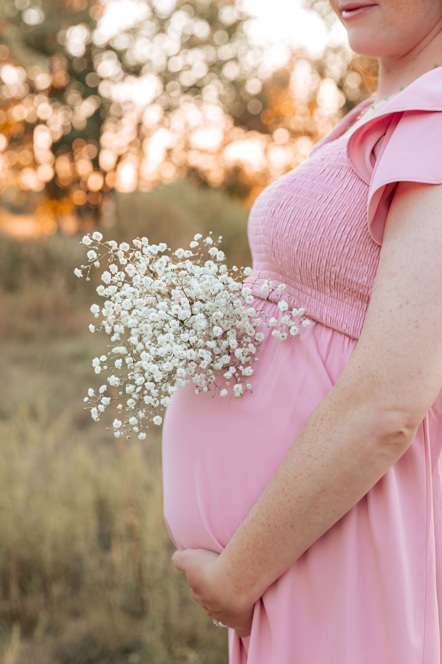Maternity photo showing baby's breath flowers held against a pink dress at sunset.