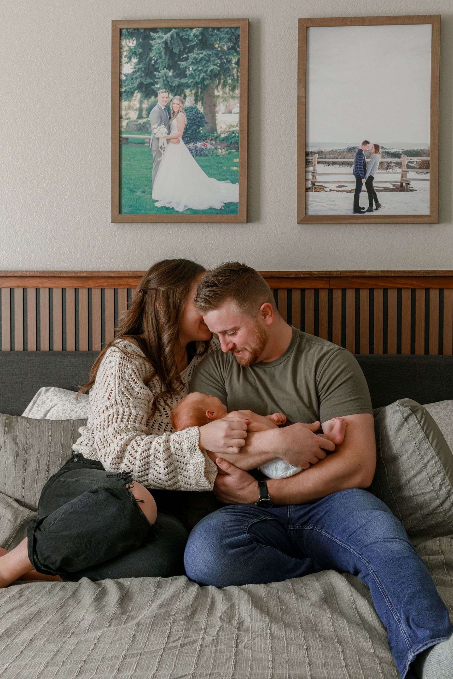 Intimate family moment captured on a grey couch with framed photos displayed on wall above.