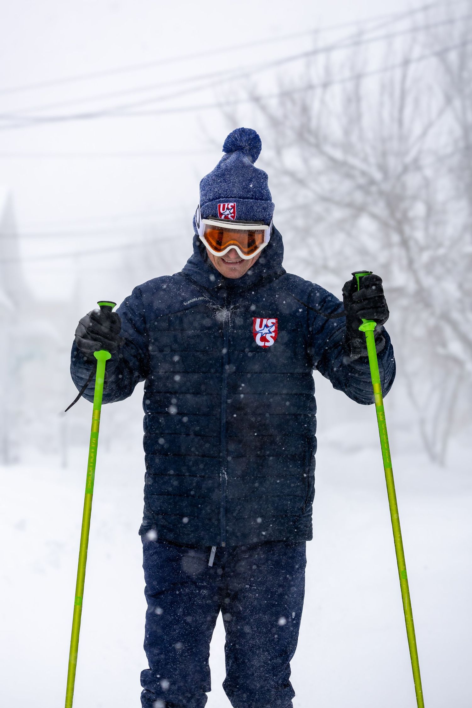 A skier in a navy snowsuit and ski goggles stands in deep powder snow during heavy snowfall.