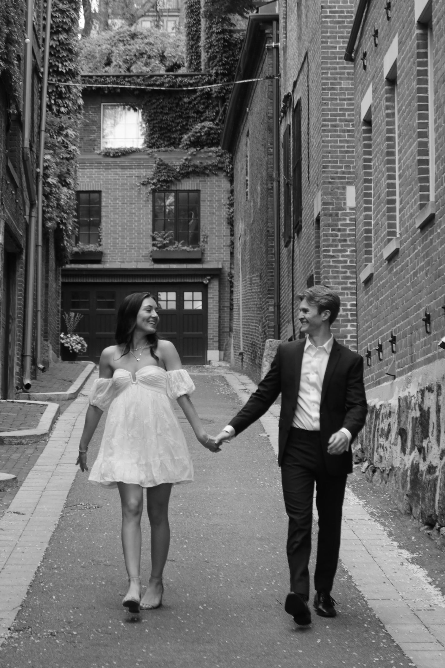 Dancing figures move gracefully through a brick-lined alleyway in black and white photography.