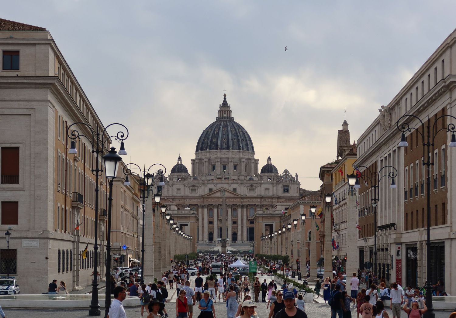 Wide view of a busy street leading to St. Peter's Basilica in Vatican City with crowds of tourists.