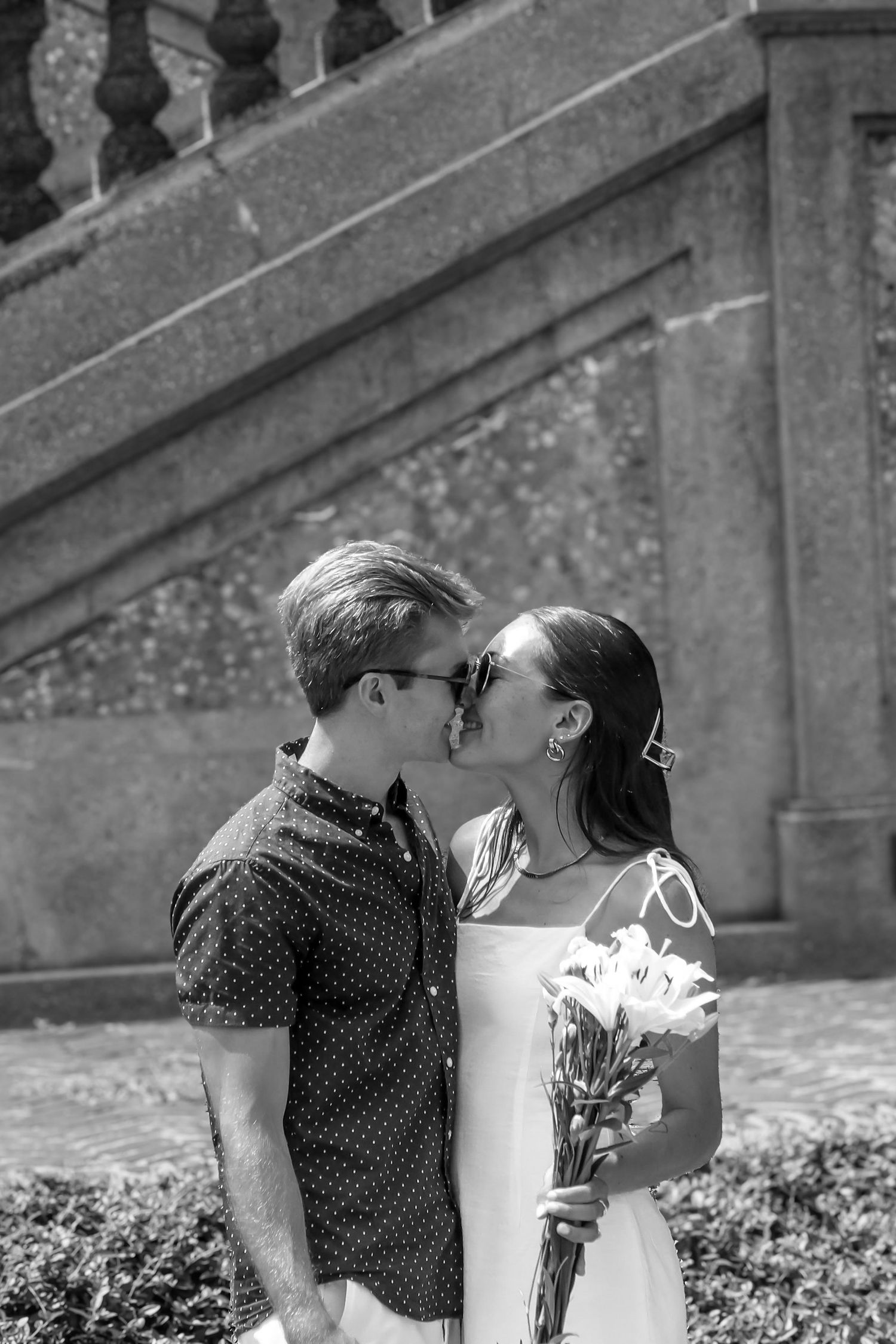 A tender embrace photographed in black and white against stone architecture.
