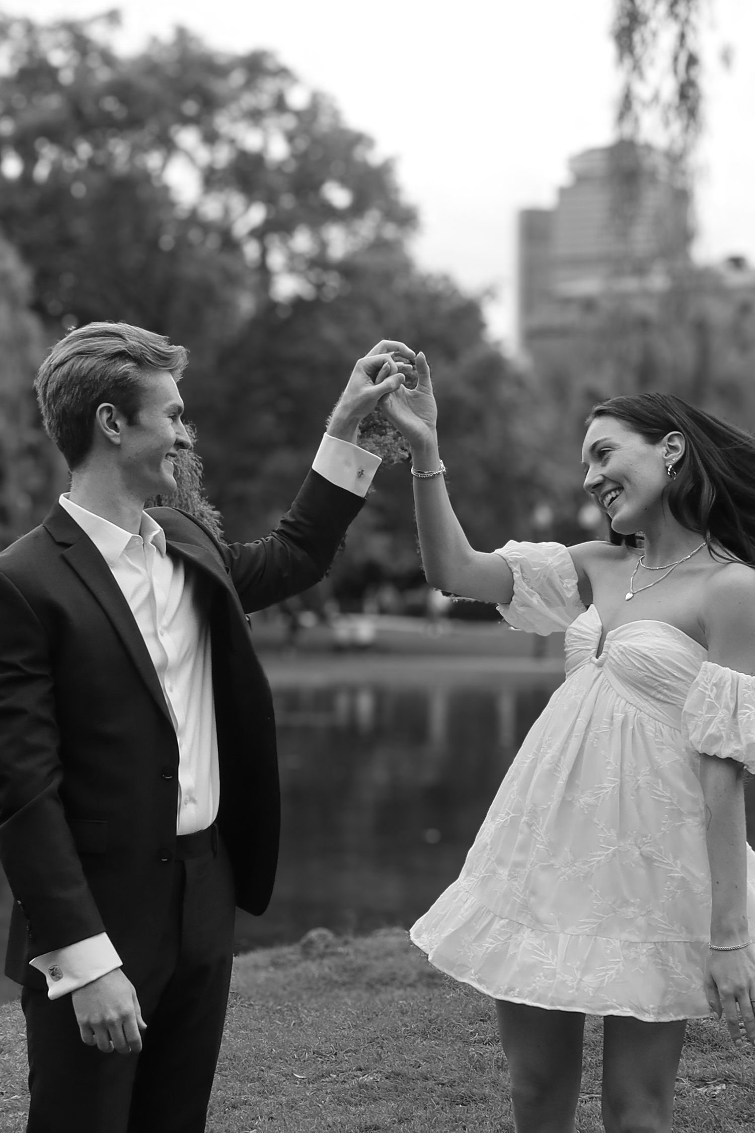 A couple in formal attire dances playfully in a park setting.