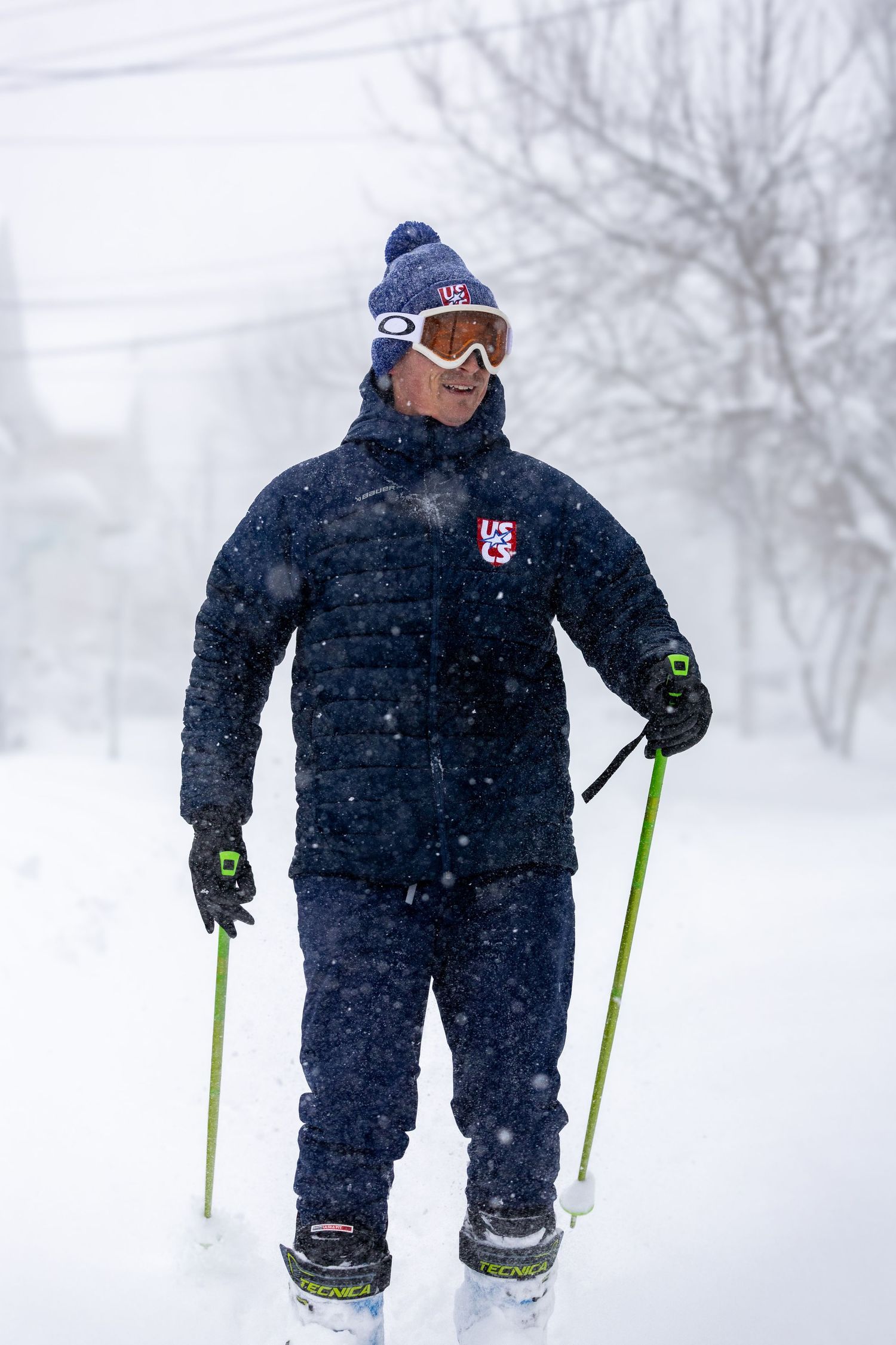 A person in dark winter gear uses bright green ski poles while navigating through snowy winter conditions.