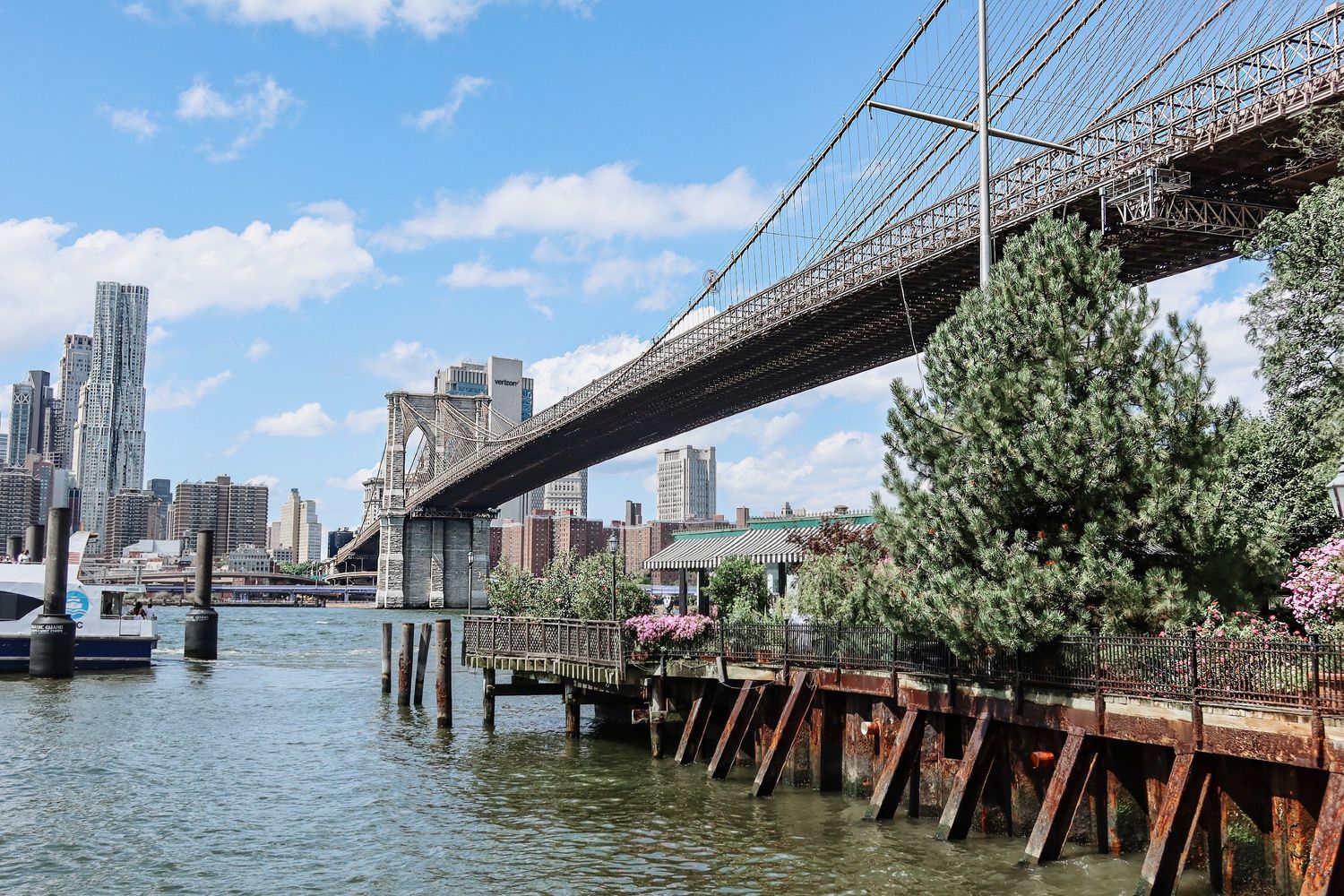 Brooklyn Bridge and Manhattan skyline viewed from waterfront on a sunny day.