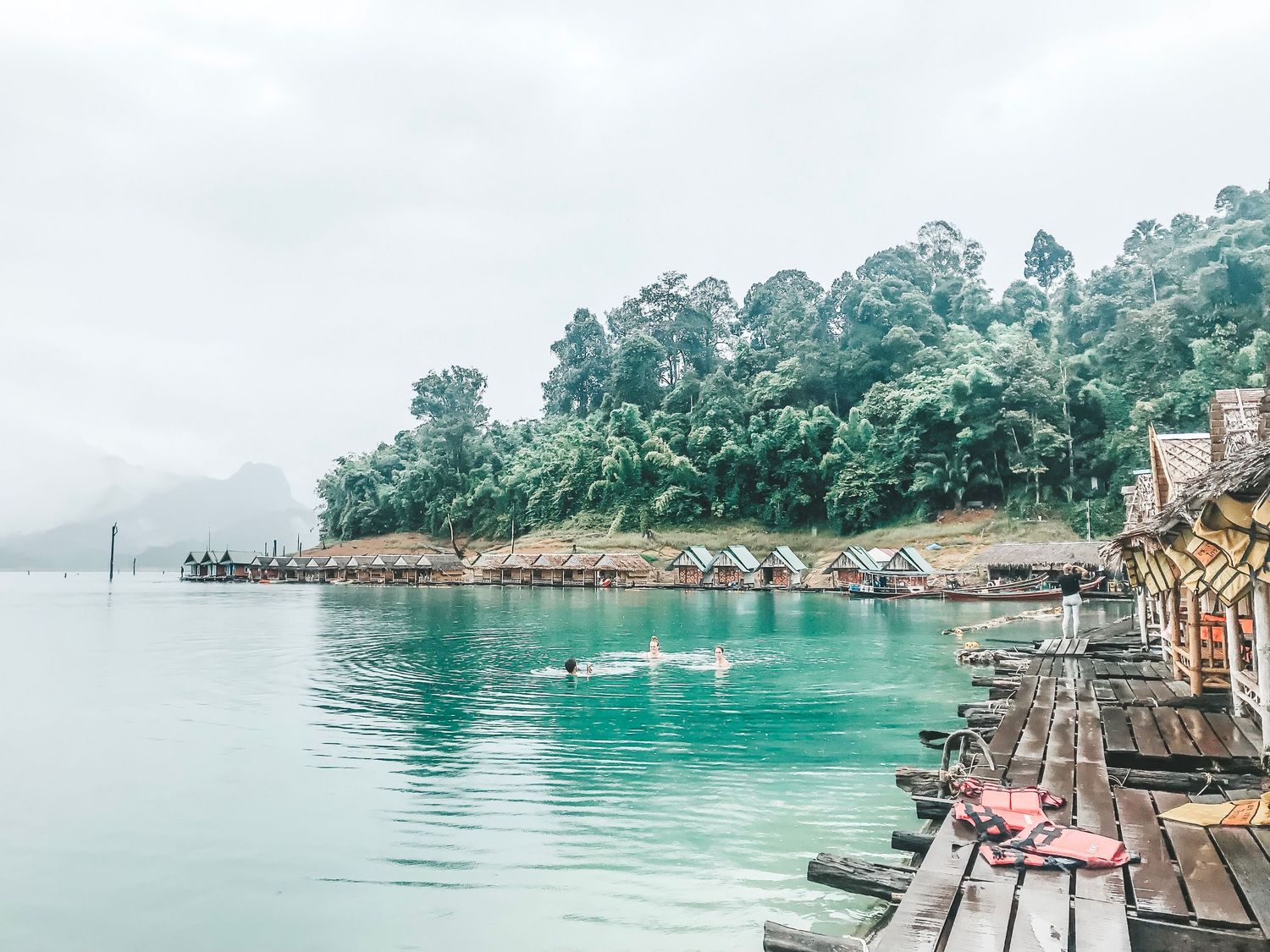 Misty lakeside view with wooden pier and colorful boathouses along the shoreline.